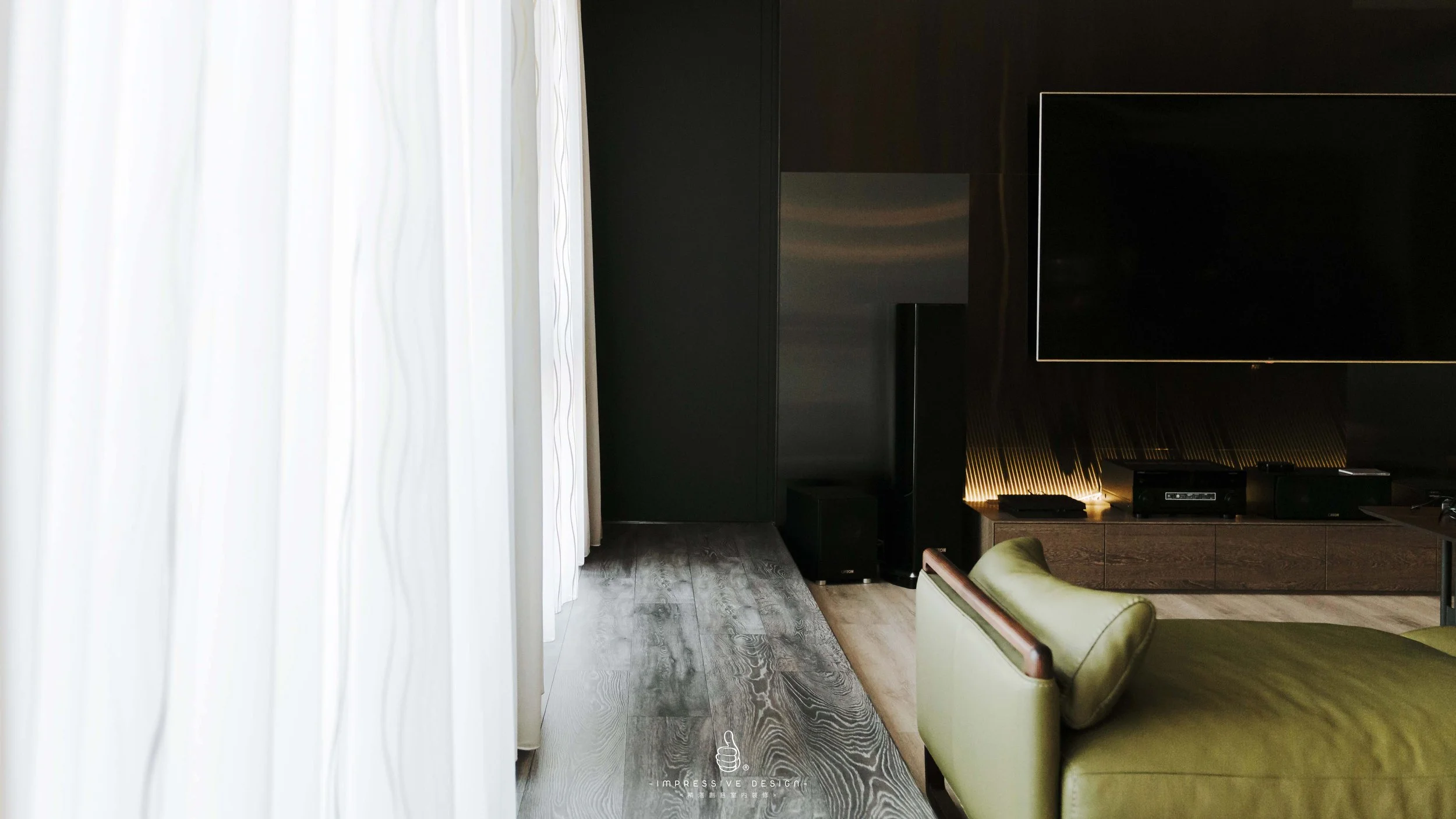 Modern living room with dark walls, a large flat-screen TV, a green armchair, and floor-to-ceiling white curtains