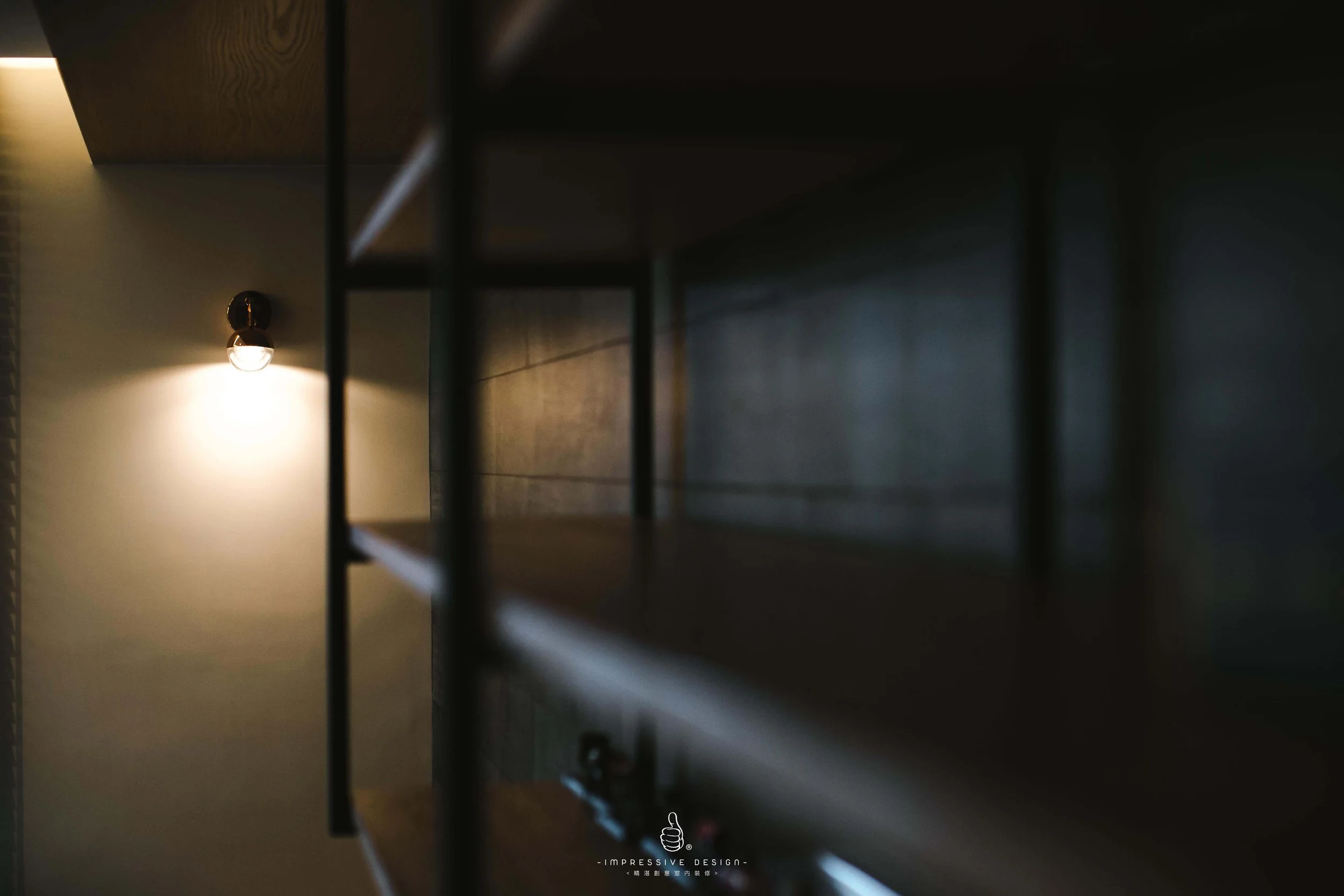 A view looking up through a dark bookshelf with a light fixture on the wall in the background, illuminating the area.