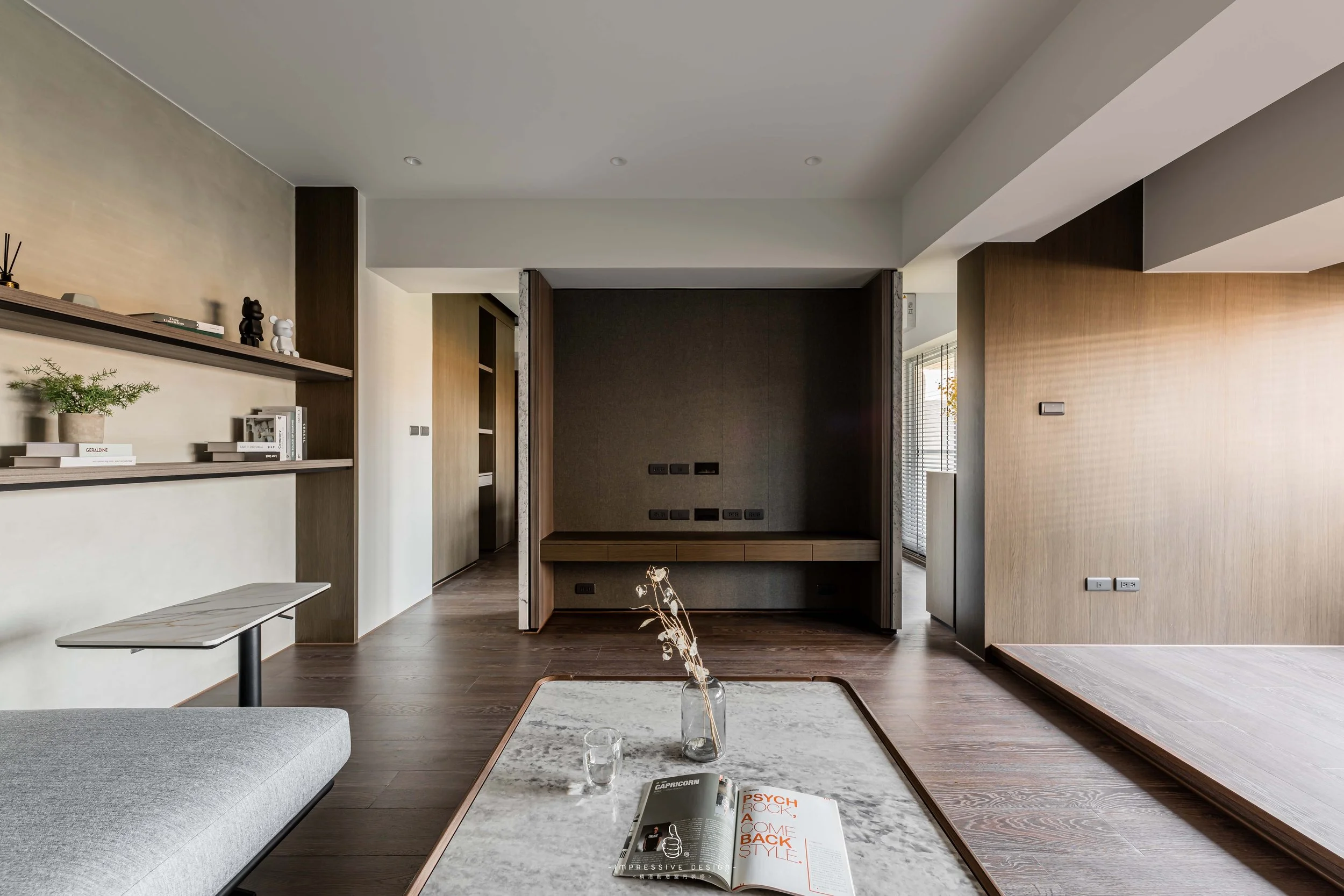 Modern living room with wooden floors, a built-in wall unit, and a coffee table with a magazine and a glass of water.