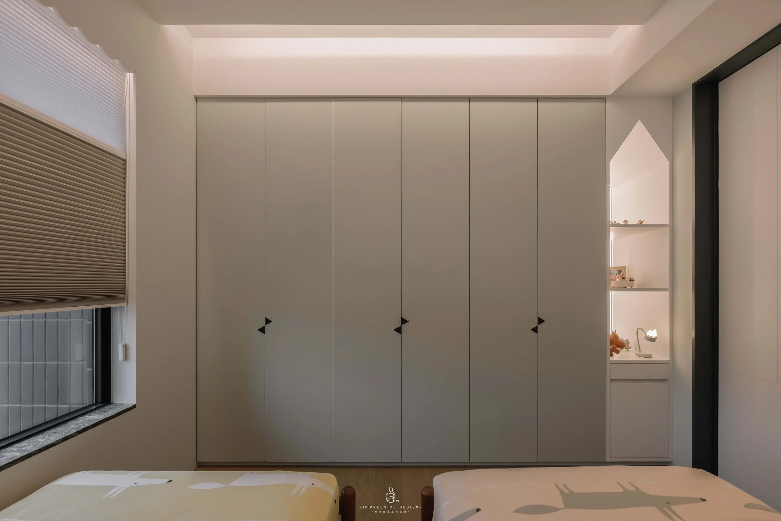 A minimalist bedroom with a large wardrobe in the center, a small window with a brown blind on the left, and a built-in shelf with decorative items on the right. The beds are partially visible at the bottom.