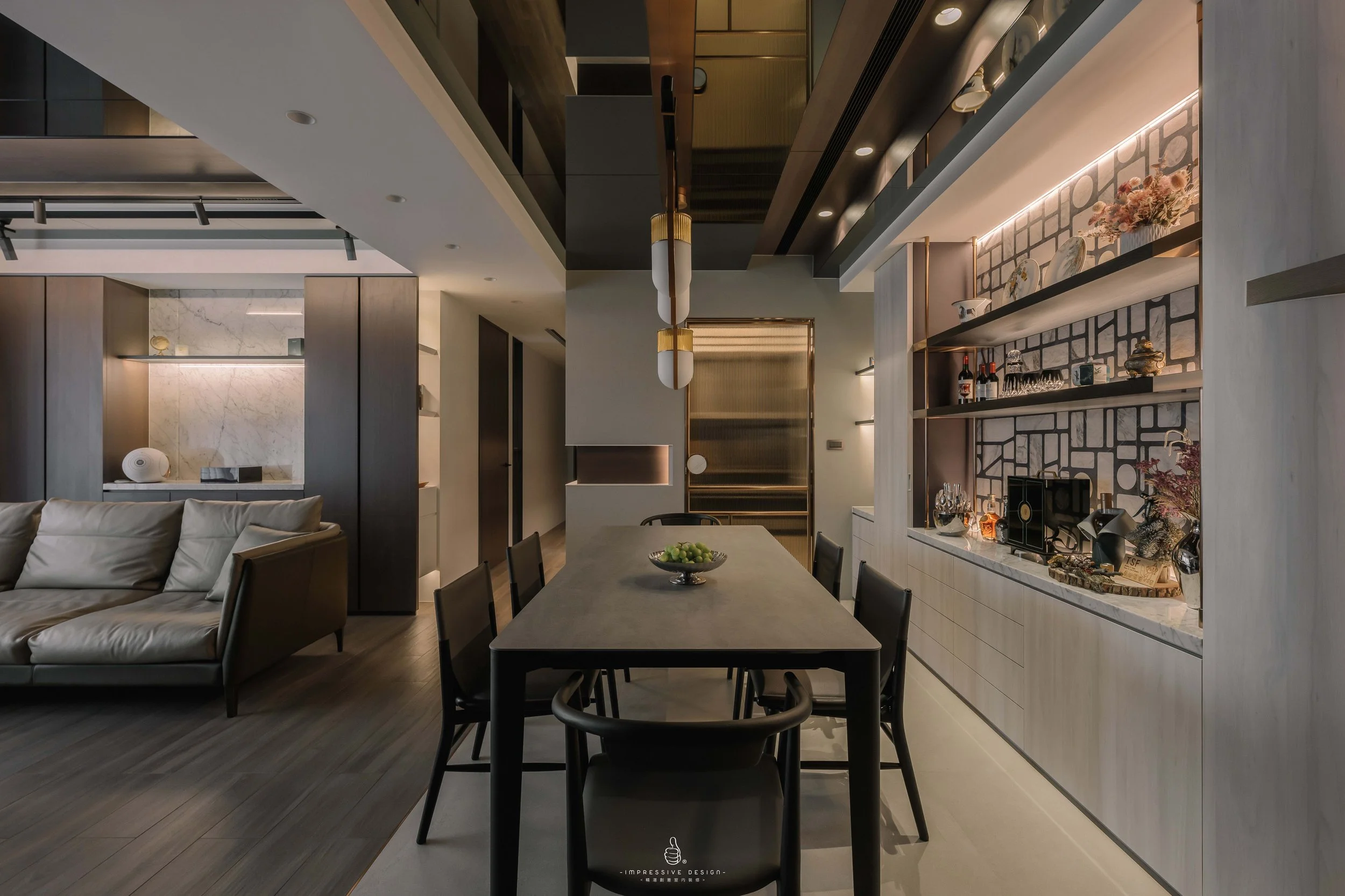 Modern dining room with a gray table, six black chairs, a built-in shelf with decorative items, a beige sofa, and contemporary lighting fixtures.