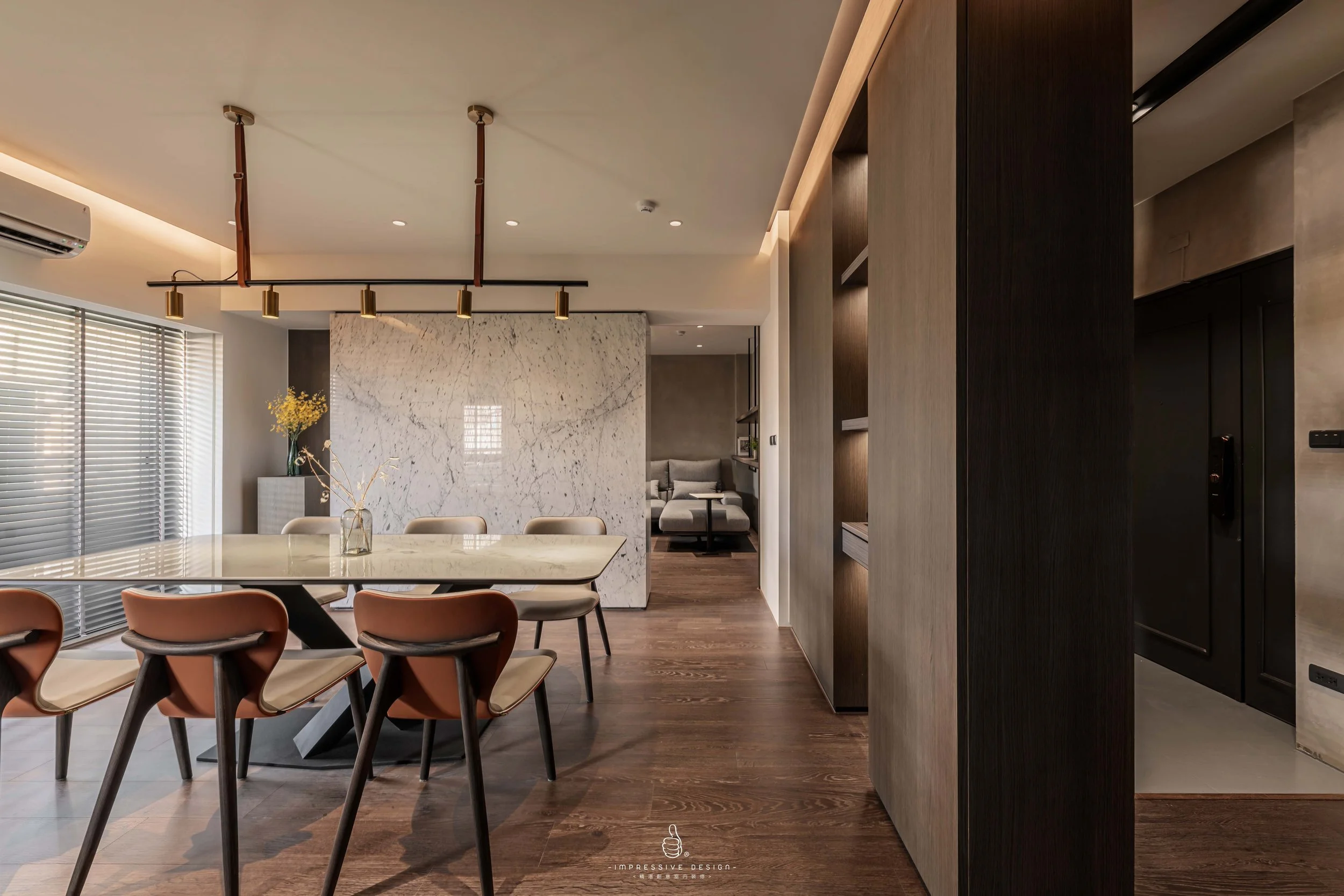 Modern dining area with a marble table, tan chairs, a marble accent wall, and a sitting area in the background.
