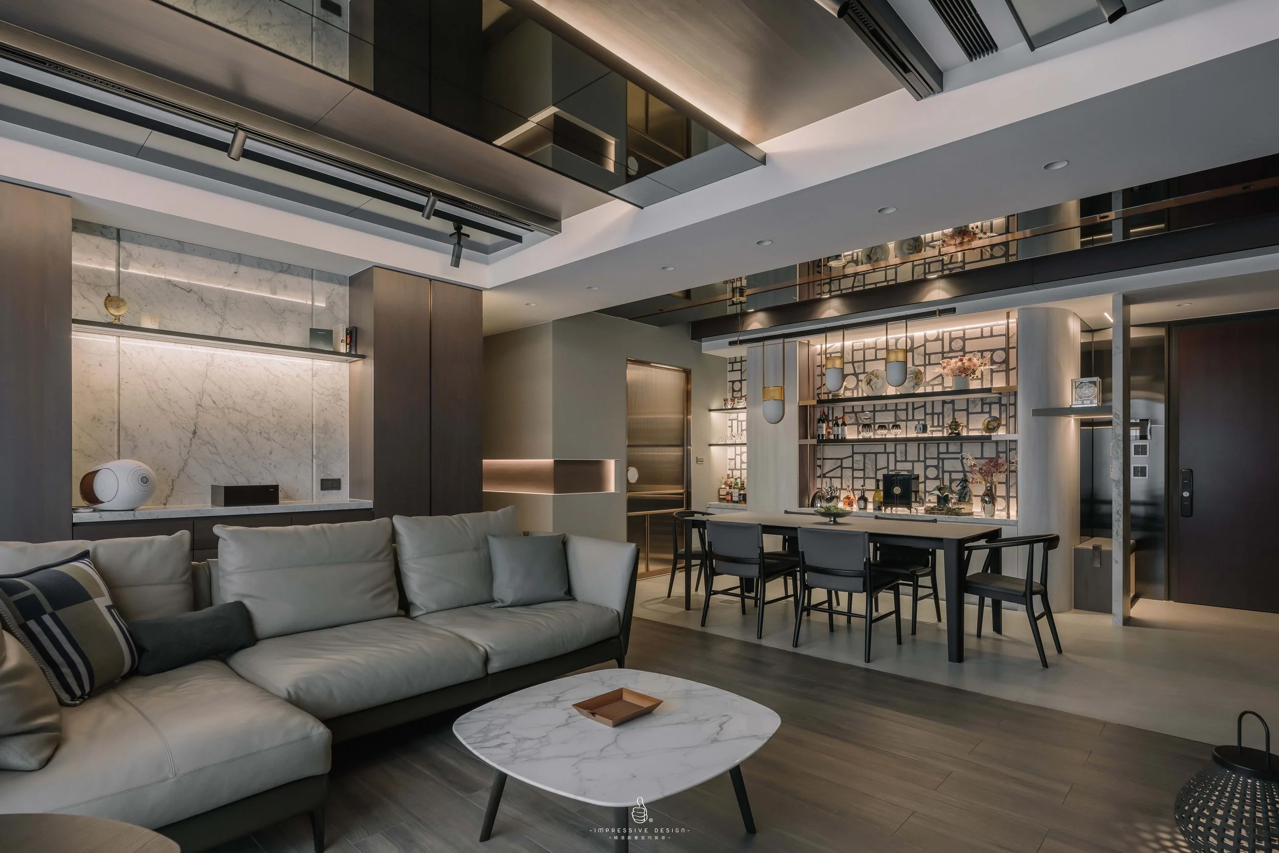 Modern living room and dining area with a white leather sofa, a marble coffee table, and a dining table with eight chairs. Shelving and decor on the wall, with a sophisticated, minimalist design.