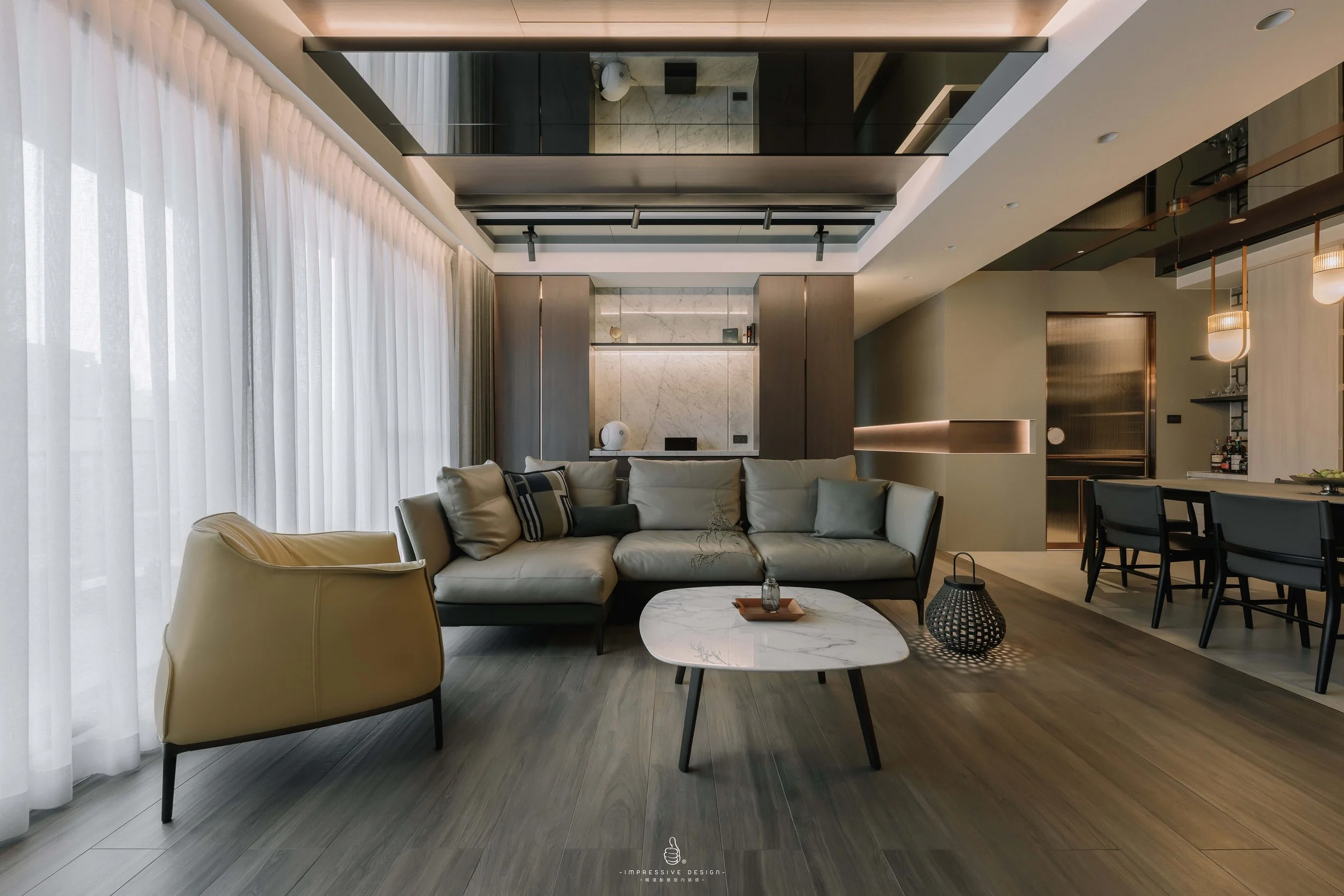 Modern living room with beige and gray furniture, a white marble coffee table, floor-to-ceiling white curtains, and a dining area in the background.
