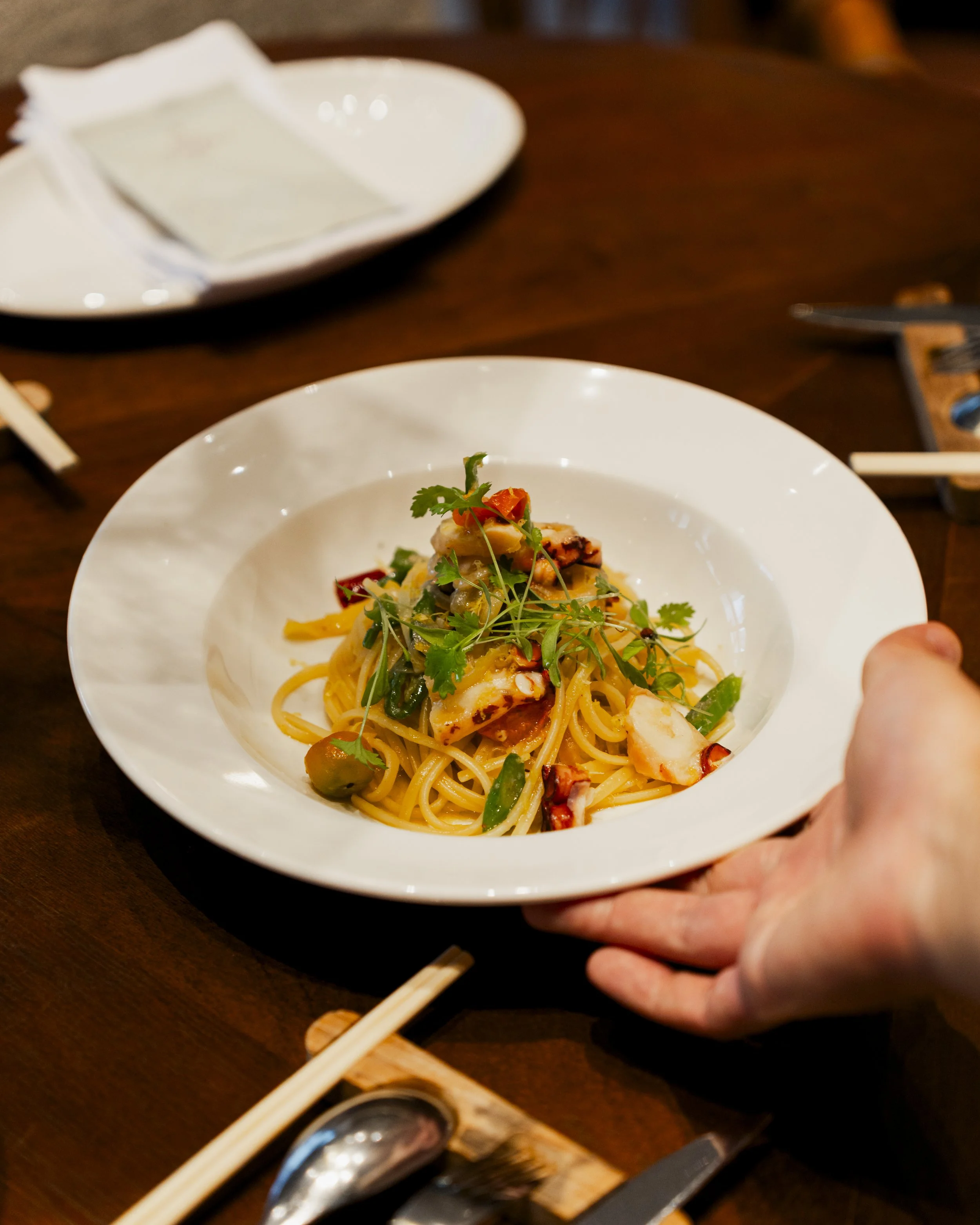 A plate of pasta with seafood, garnished with fresh herbs, on a dark wooden table.
