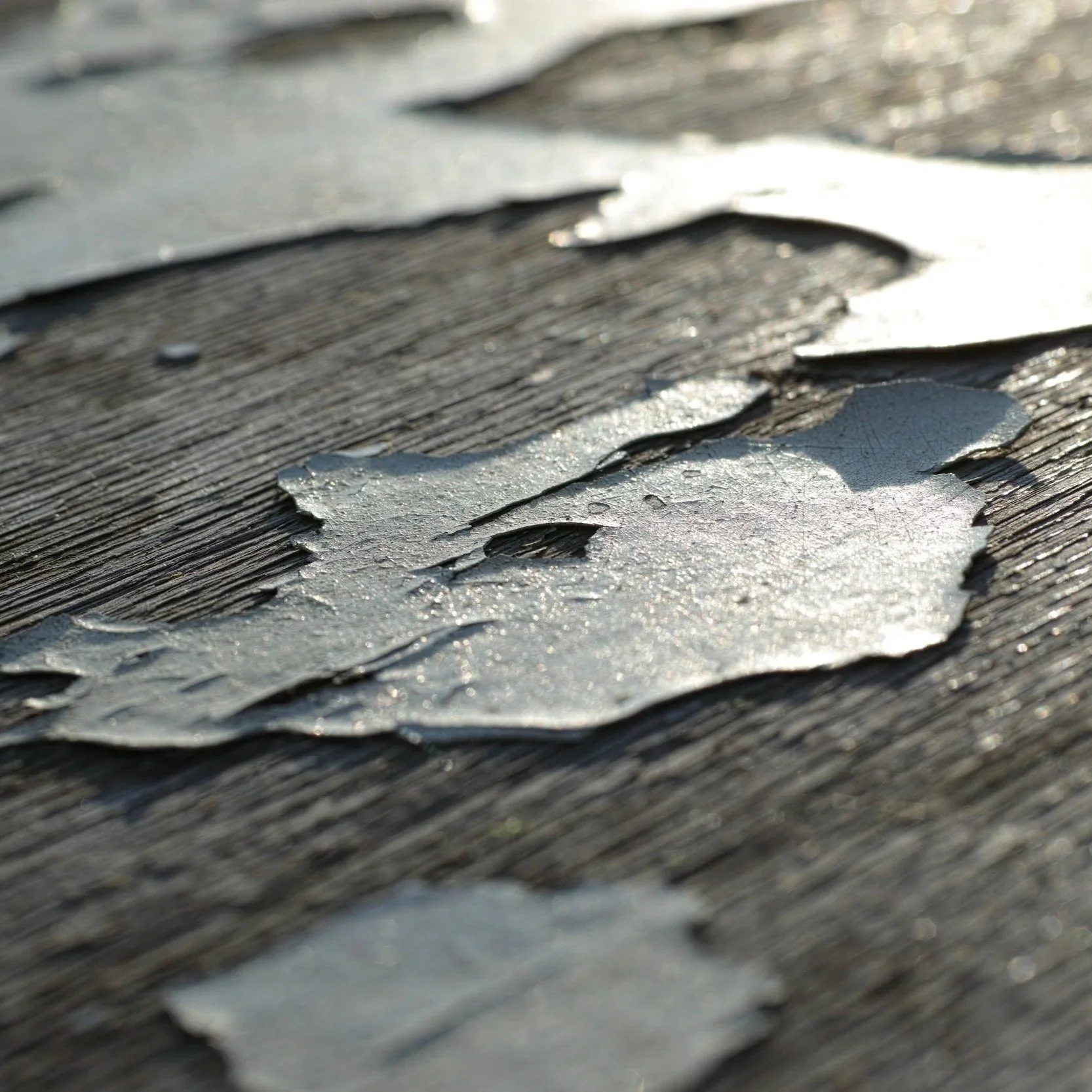 Close-up of severely deteriorated roof shingles peeling away from weathered wooden decking, exposing the surface to water damage and leaks.