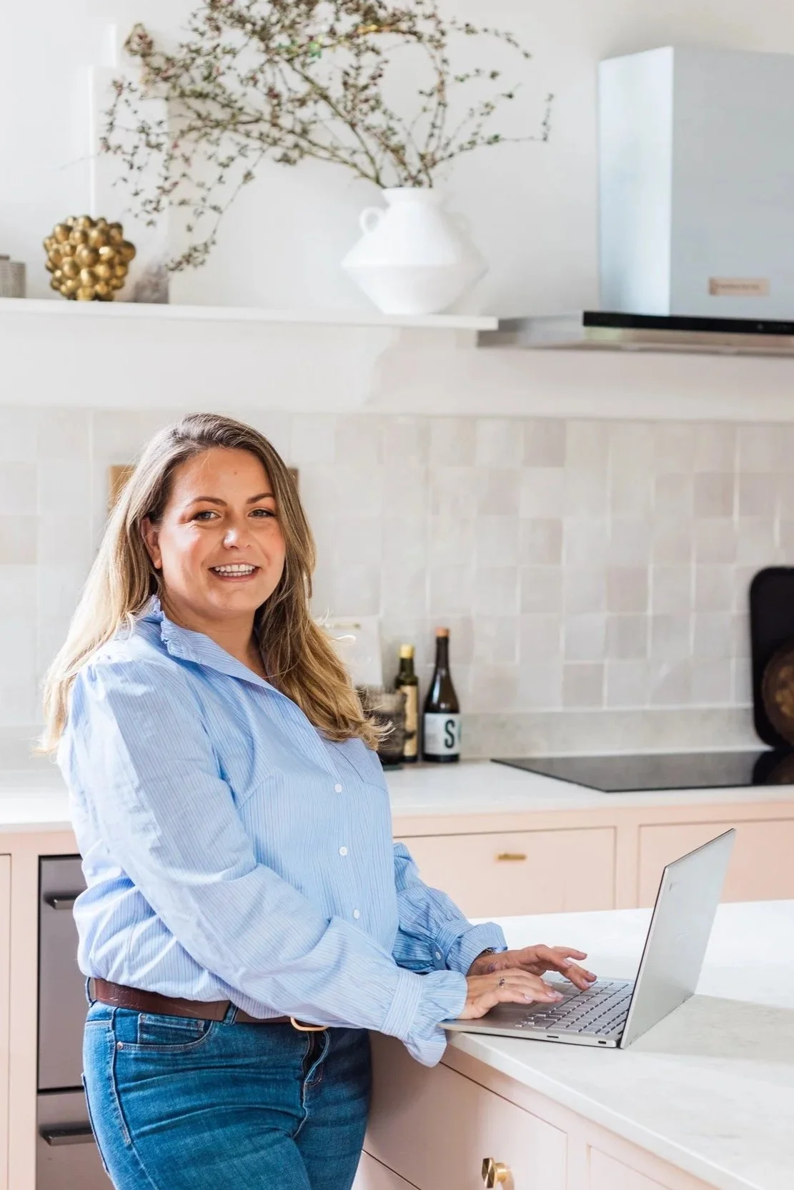 Holistic baby sleep consultant Keri Rock working on a laptop in a bright kitchen, providing expert sleep advice and support for parents.