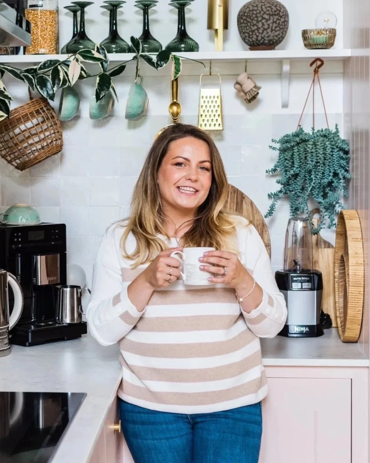 Baby sleep consultant Keri Rock, founder of Sleepy Mums, standing in a bright kitchen holding a cup of tea, representing her gentle and relatable approach to sleep coaching.