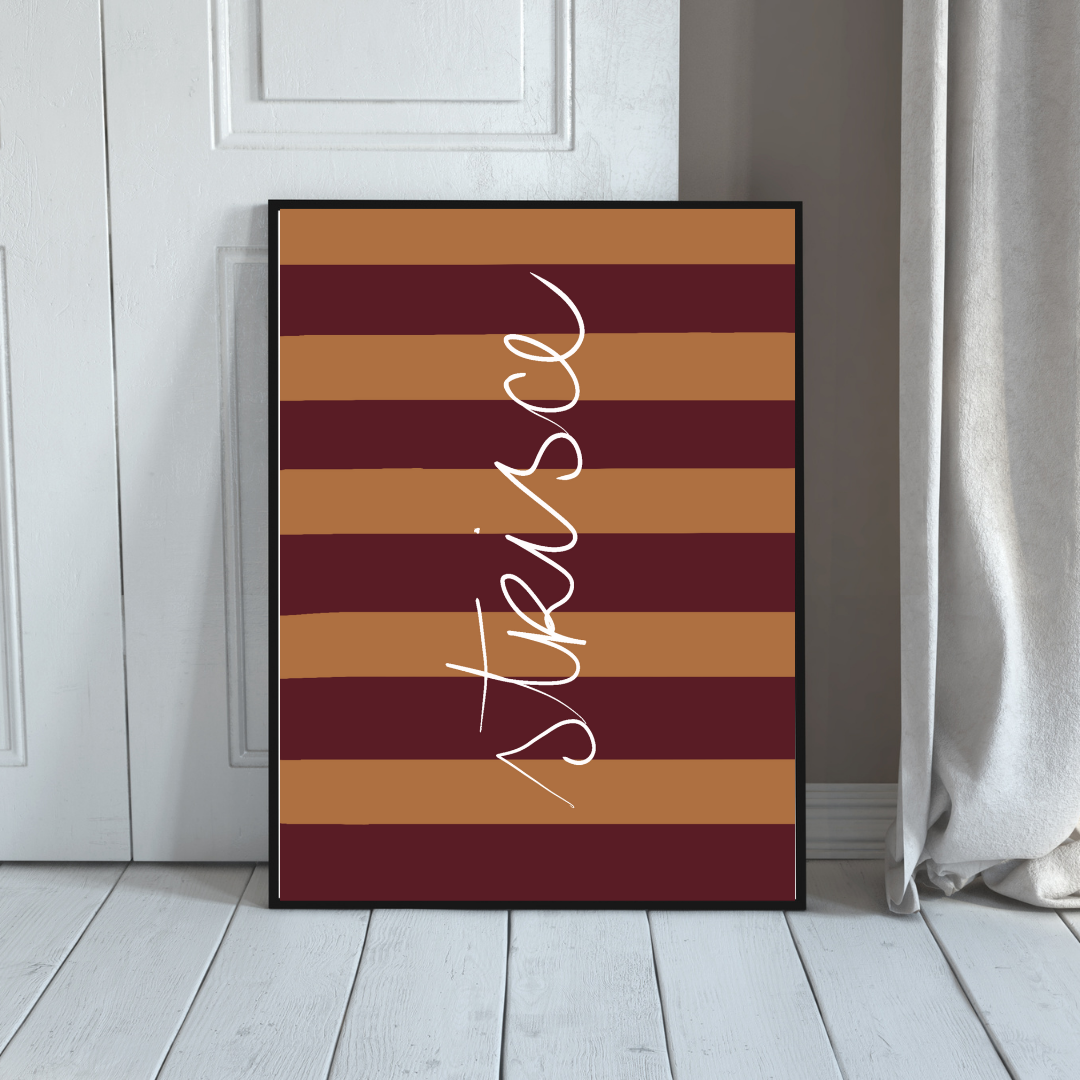 Decorative framed poster with horizontal brown and maroon stripes and the word 'Thankful' written vertically in white cursive, leaning against a white wall near a white door and curtains.