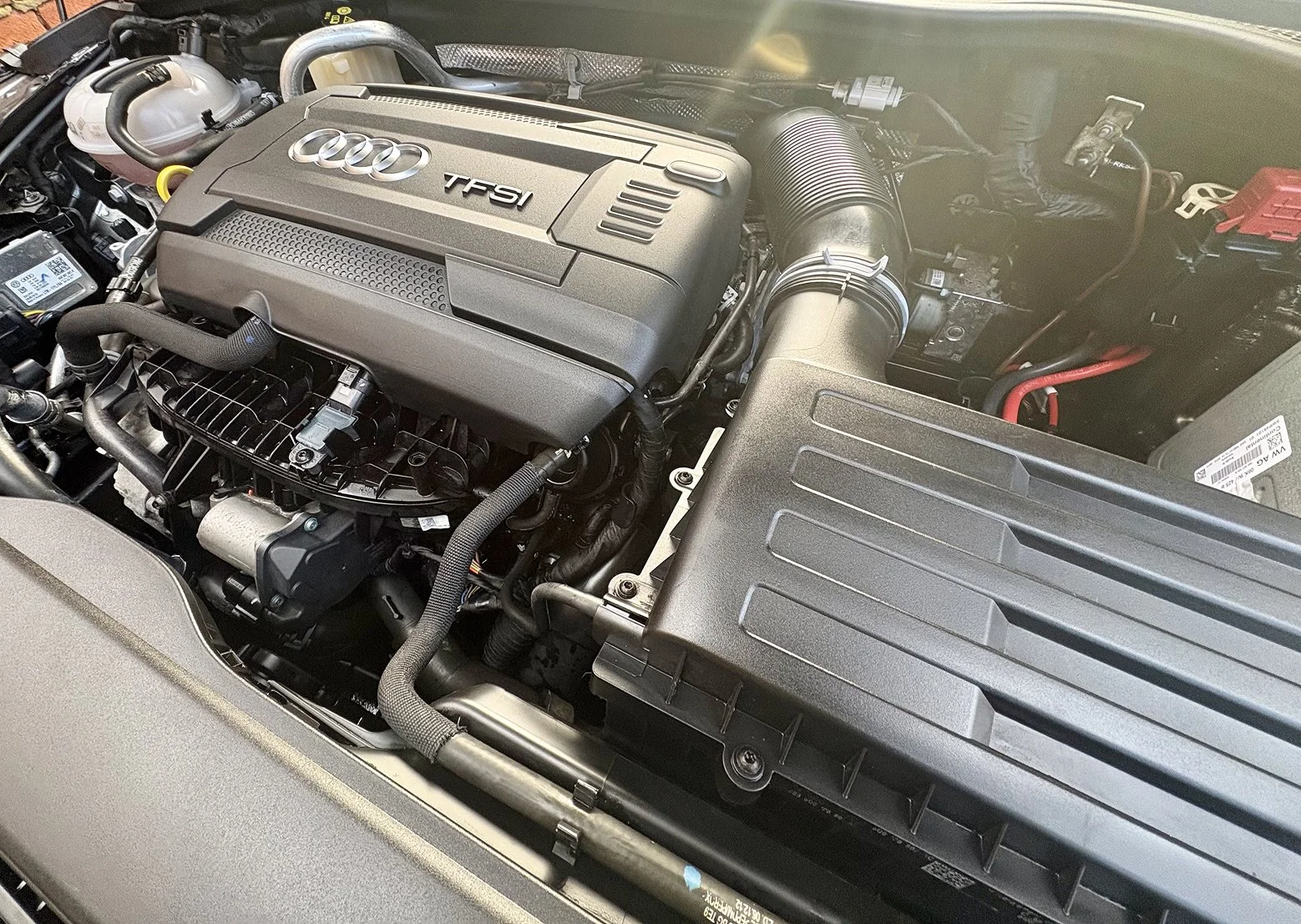 Close-up of an Audi car engine with TFSI badge, various hoses, and components visible underneath the hood.