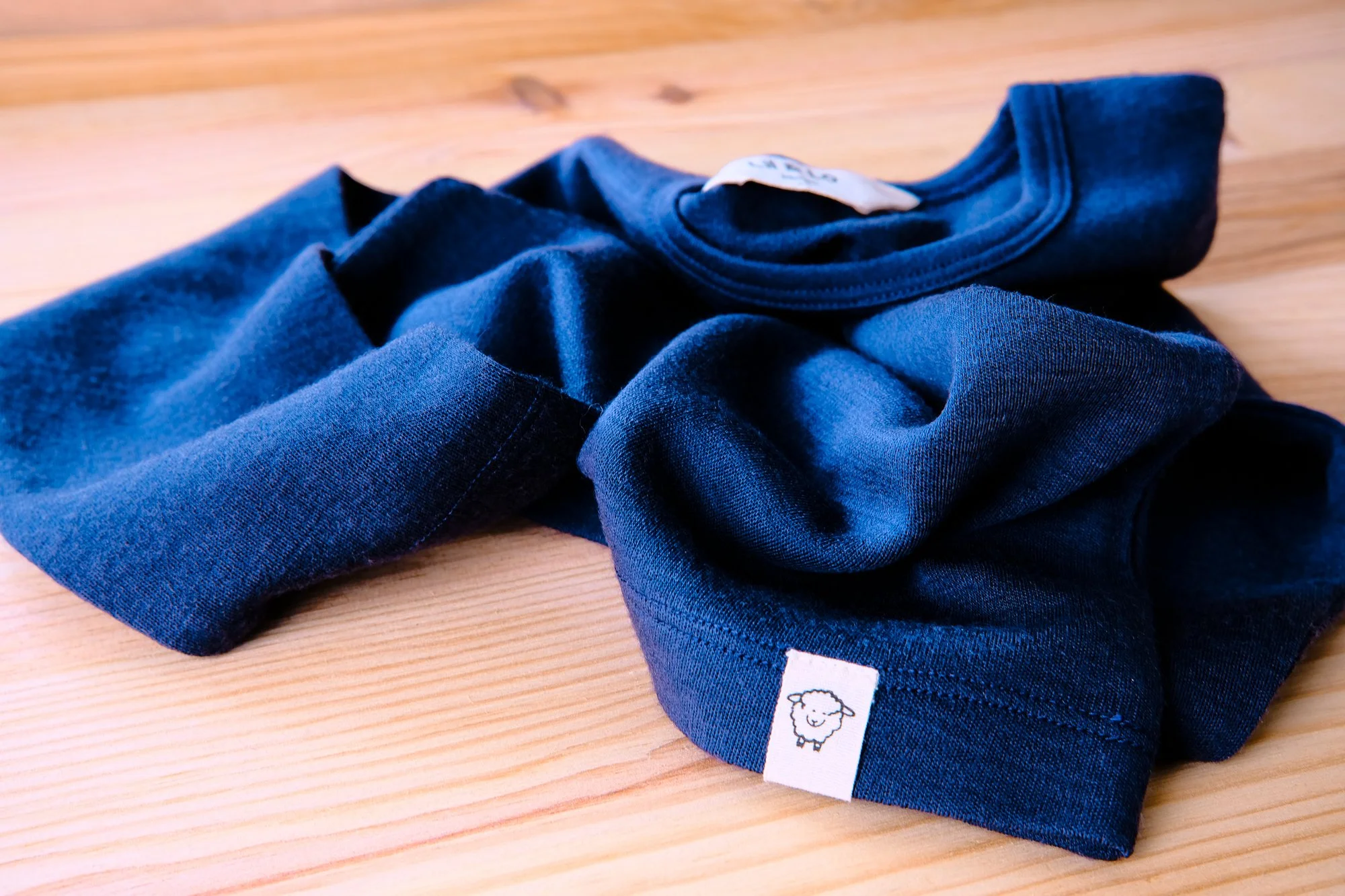 A folded navy blue T-shirt and a navy blue sock with a small sheep logo, placed on a wooden surface. Product photography fashion photography for childrens brands.