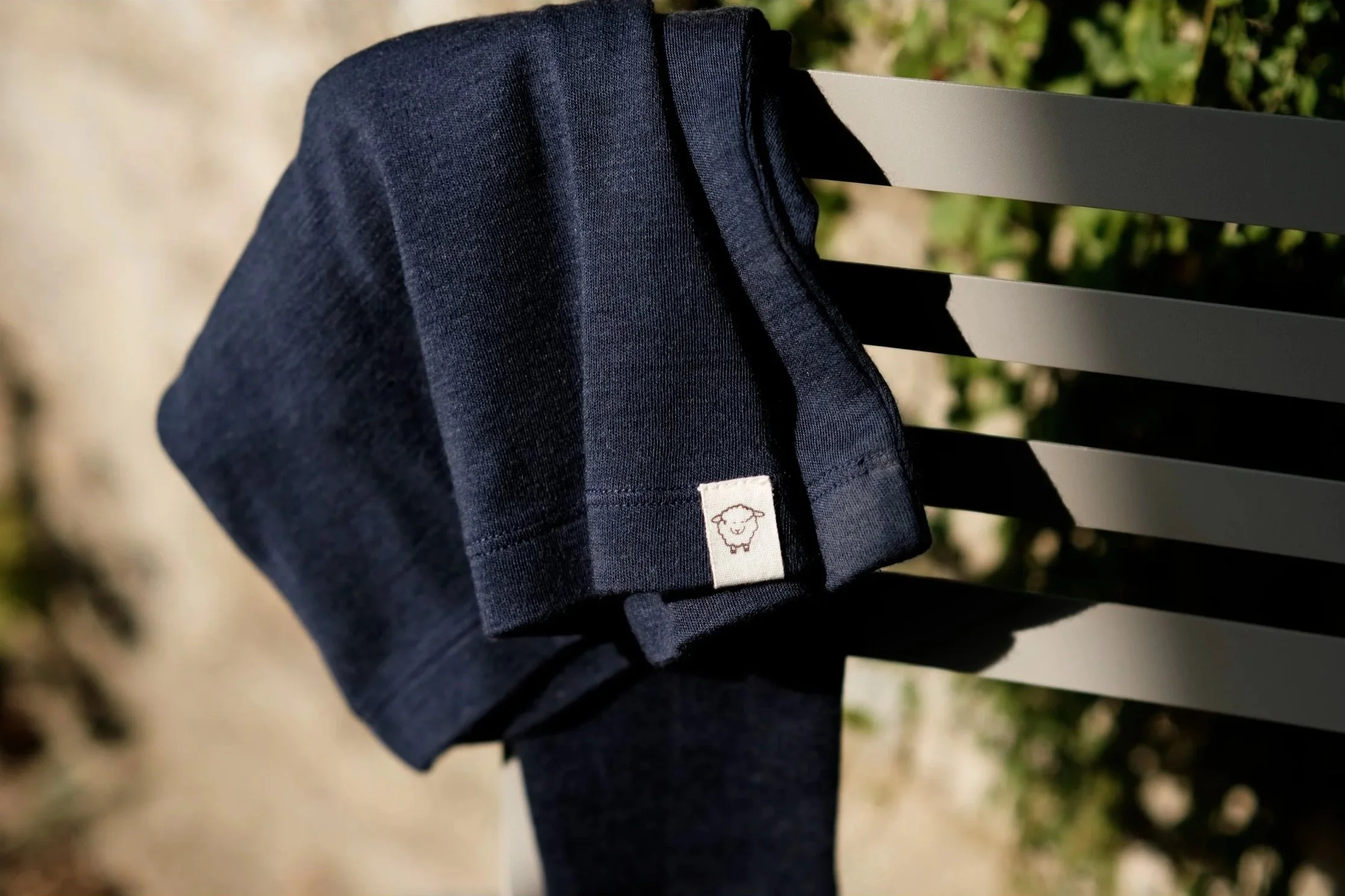 A dark blue t-shirt draped over a gray outdoor chair with a cartoon sheep logo on the sleeve. outdoor product photography children's fashion brand photographer childrenswear clothing