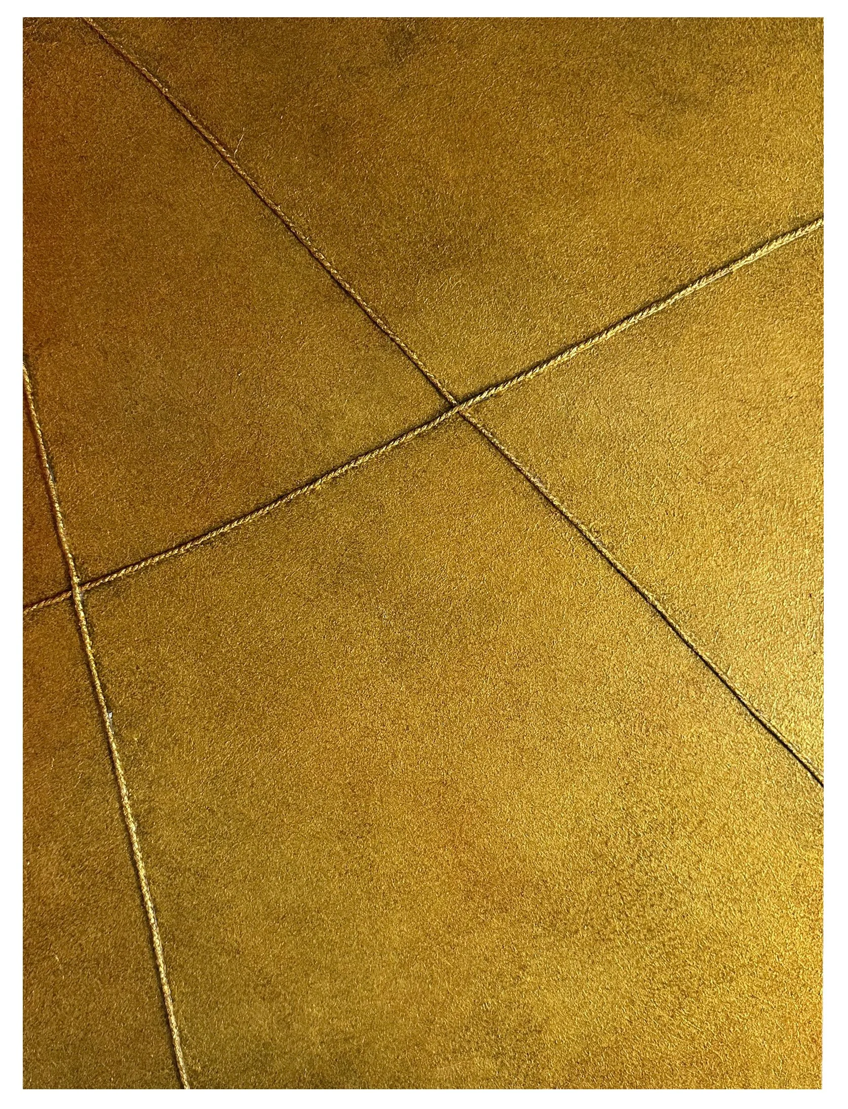 Close-up of a gold-colored leather or faux leather surface with visible stitching forming a grid pattern.