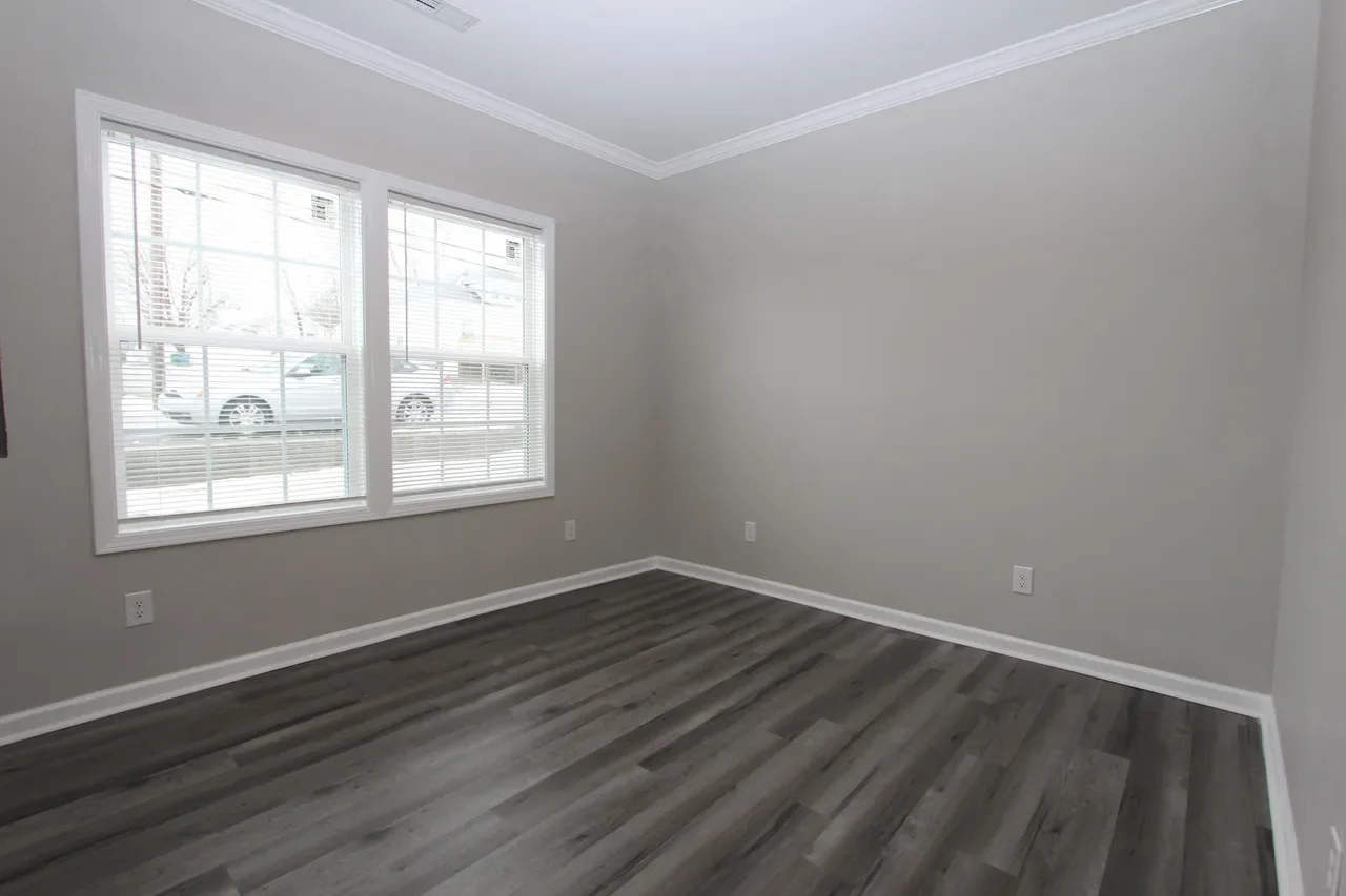 Empty room with gray walls, dark gray flooring, white trim, and two large windows with blinds.