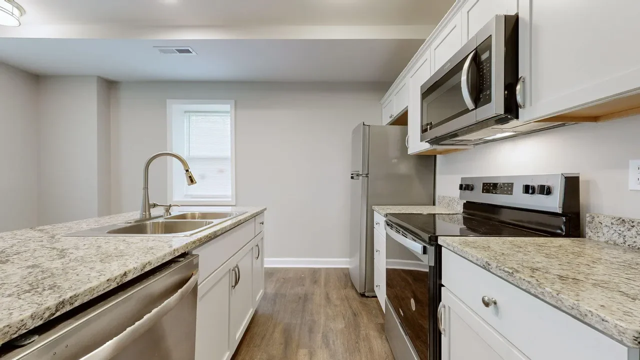 Modern kitchen with white cabinets, granite countertops, stainless steel appliances including a microwave, refrigerator, and oven, and hardwood flooring.