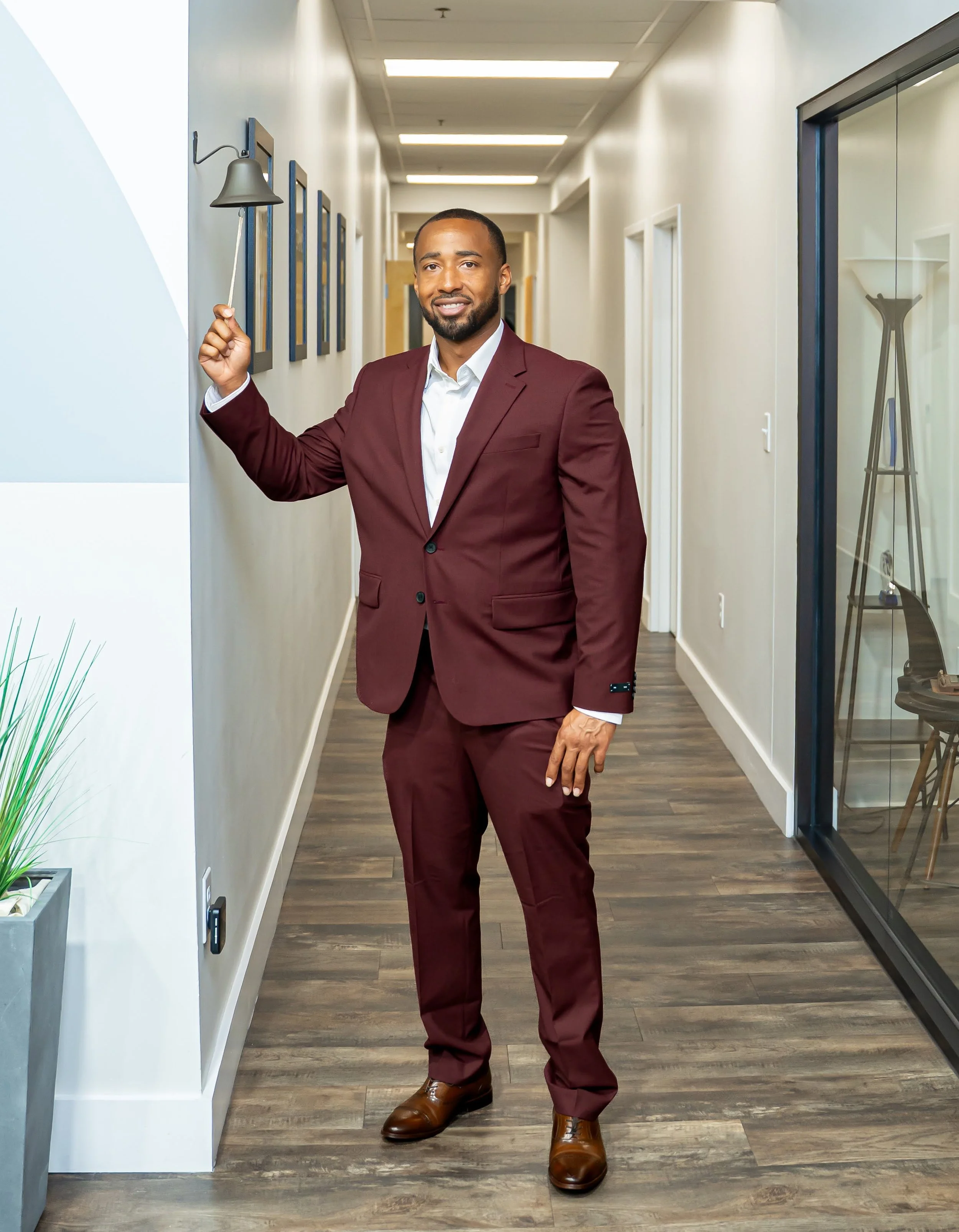 Lance Morton standing in a hallway at Guide Realty and ringing a small bell near framed pictures on the wall.