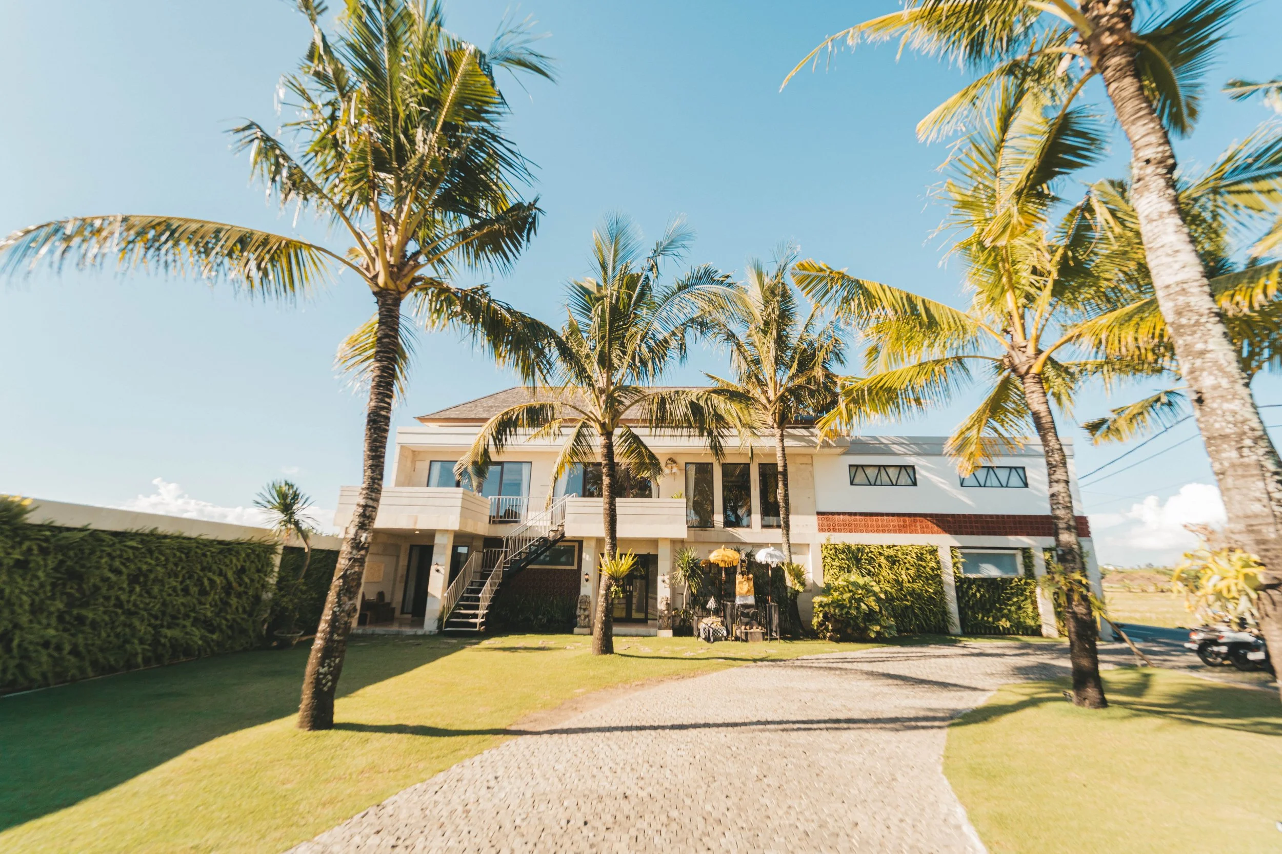Front view of a modern house with palm trees, a green lawn, and clear sky in the background.