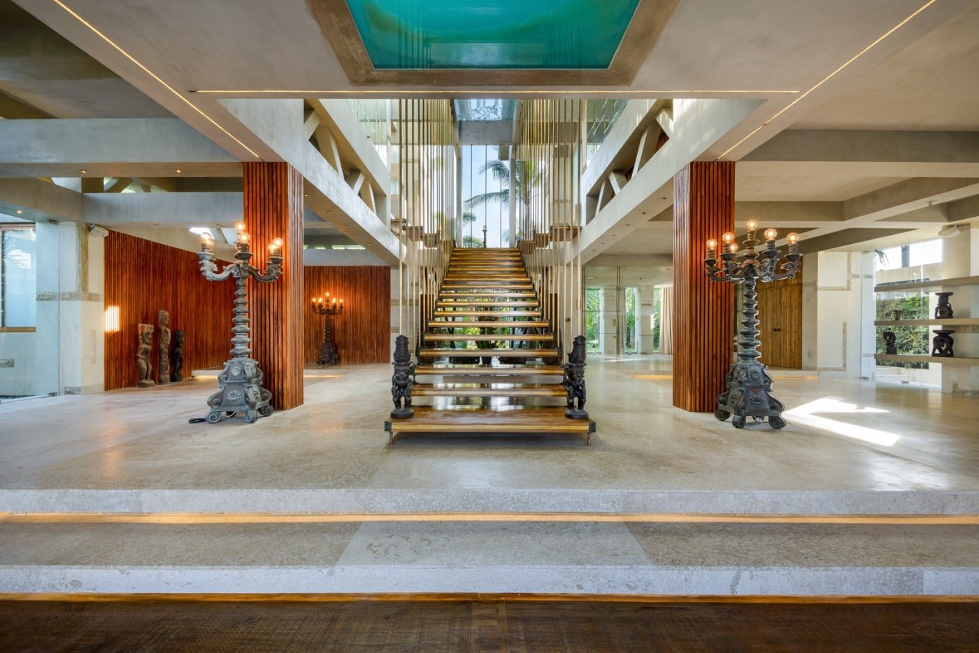 Modern lobby with wooden staircase, decorative statues, and candelabra-style lamps.