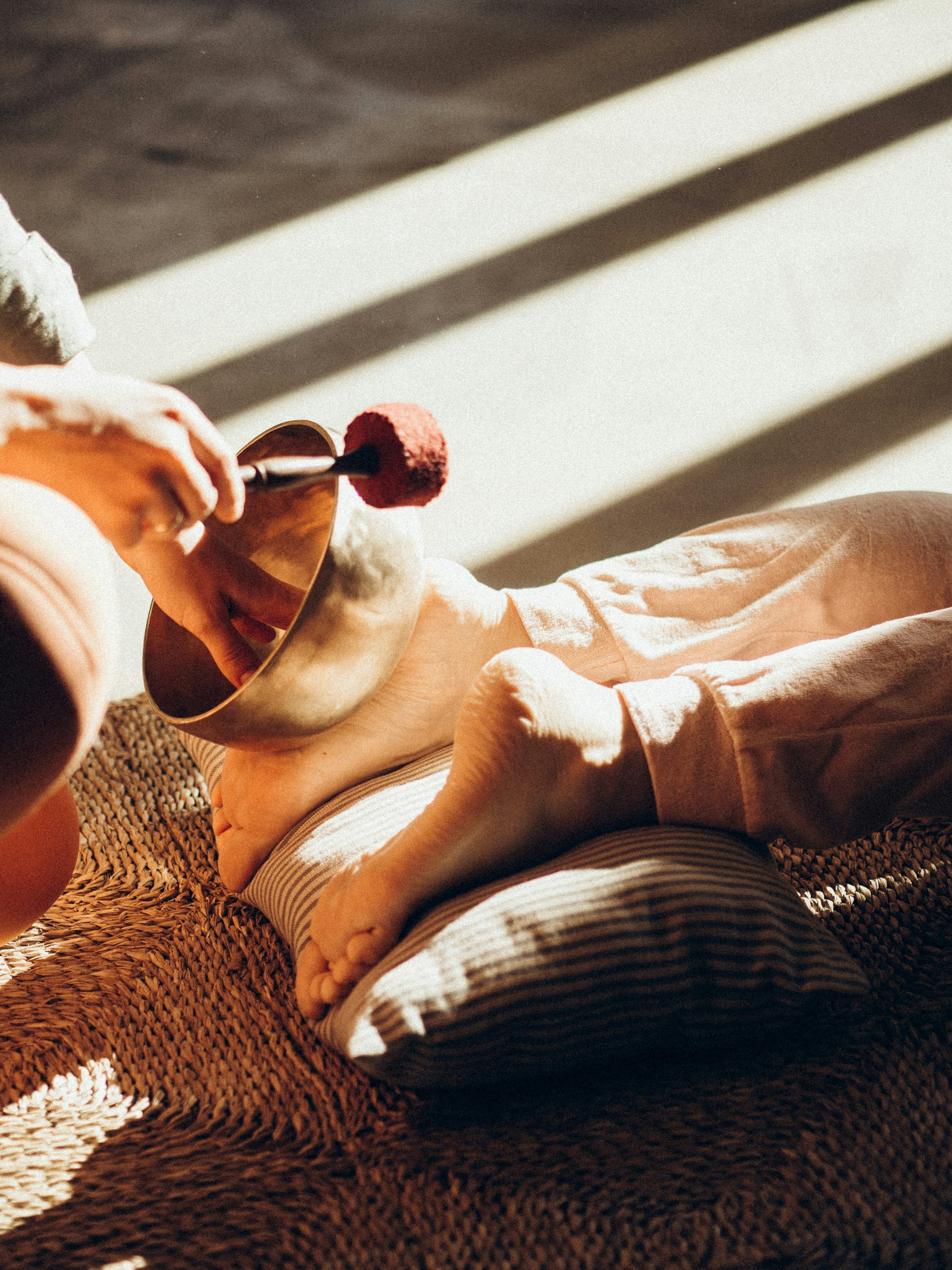 Sound healer uses a sound bowl near the feet of a client, with beautiful warm light