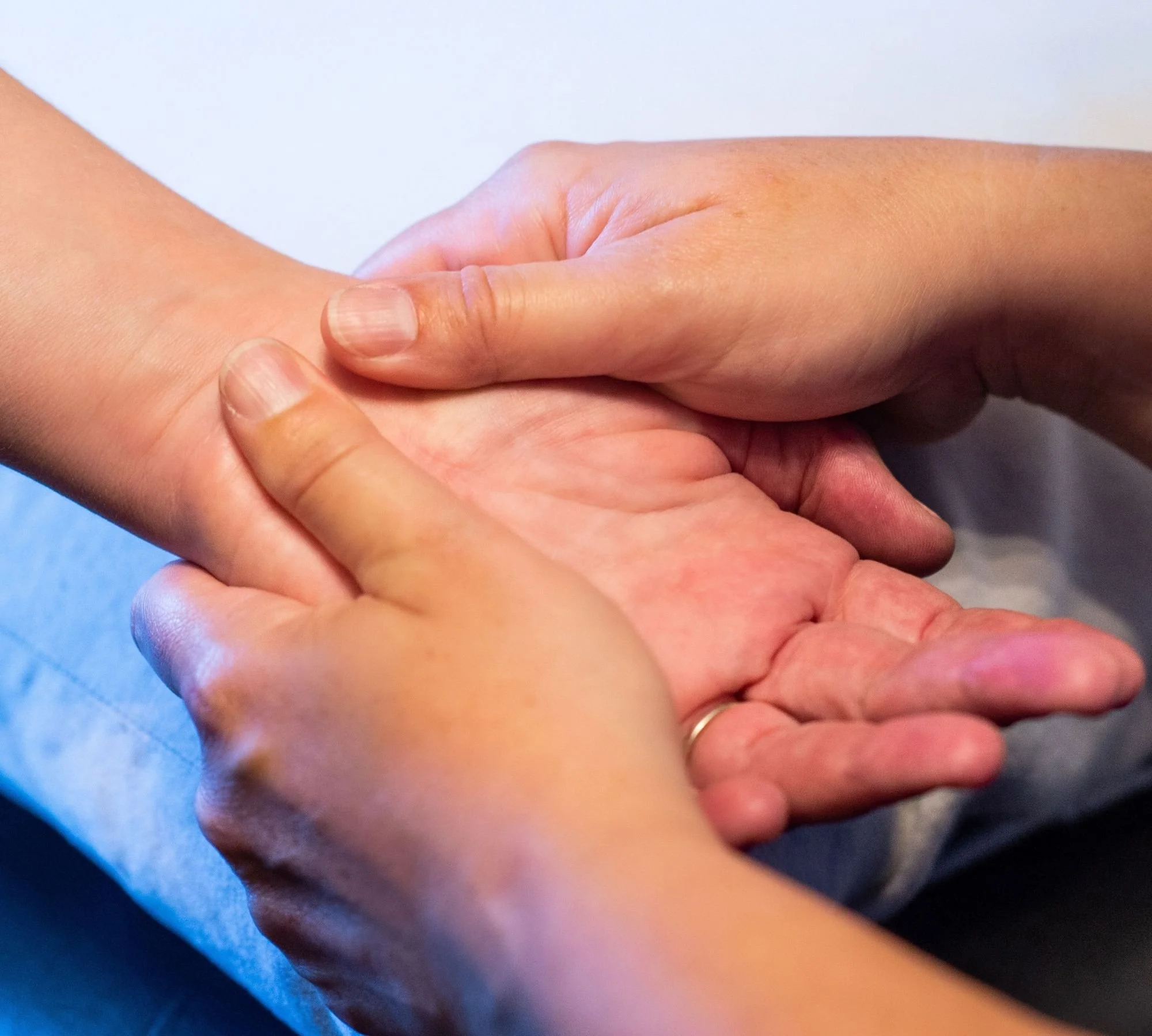 Two hands holding each other, with one hand gently gripping the other's wrist.