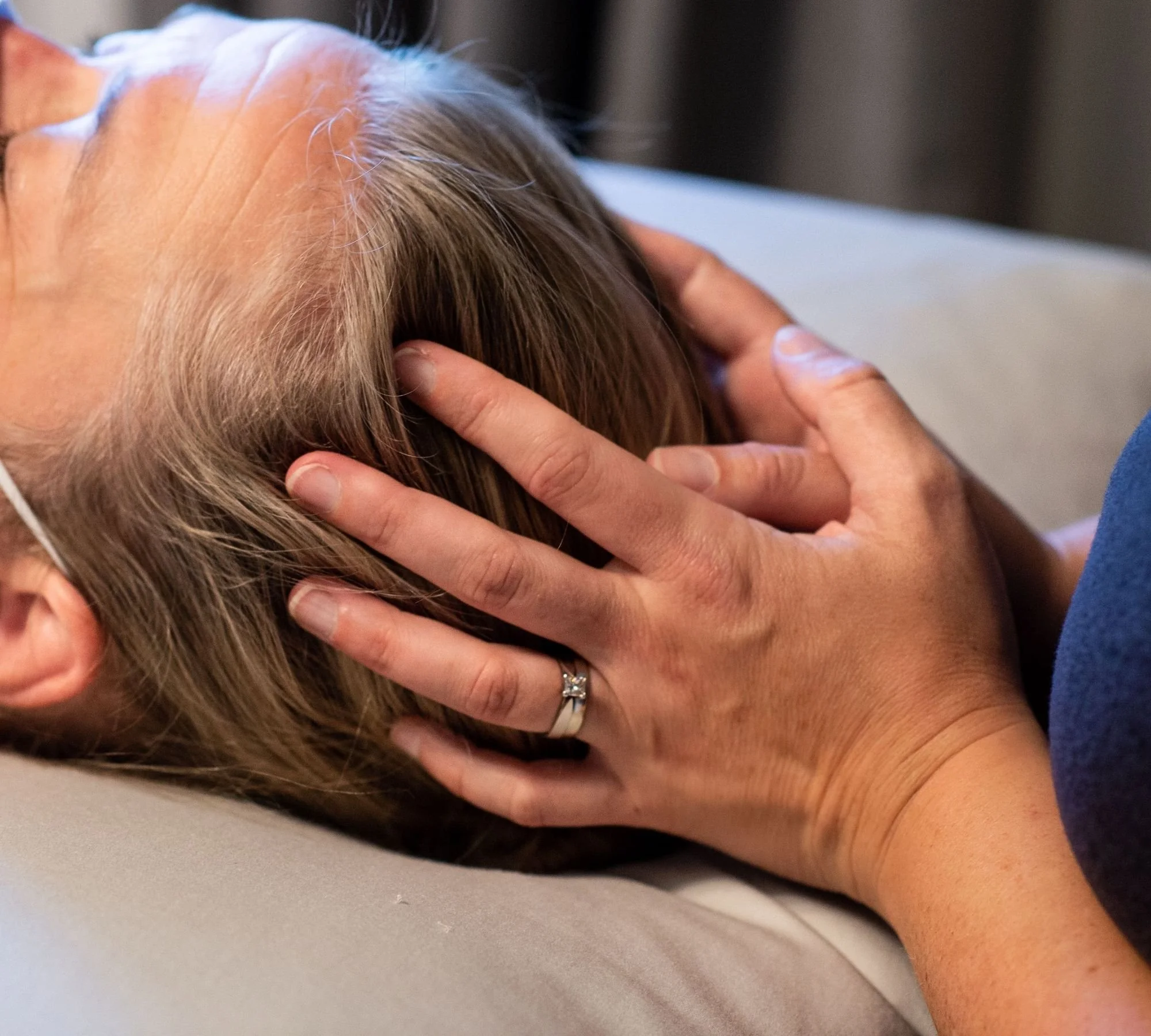 Close-up of a person receiving a head massage, with hands gently holding the person's head and fingers resting on scalp, wearing a wedding ring.