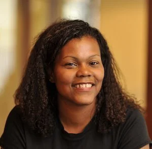 A woman with curly hair smiling at the camera indoors.