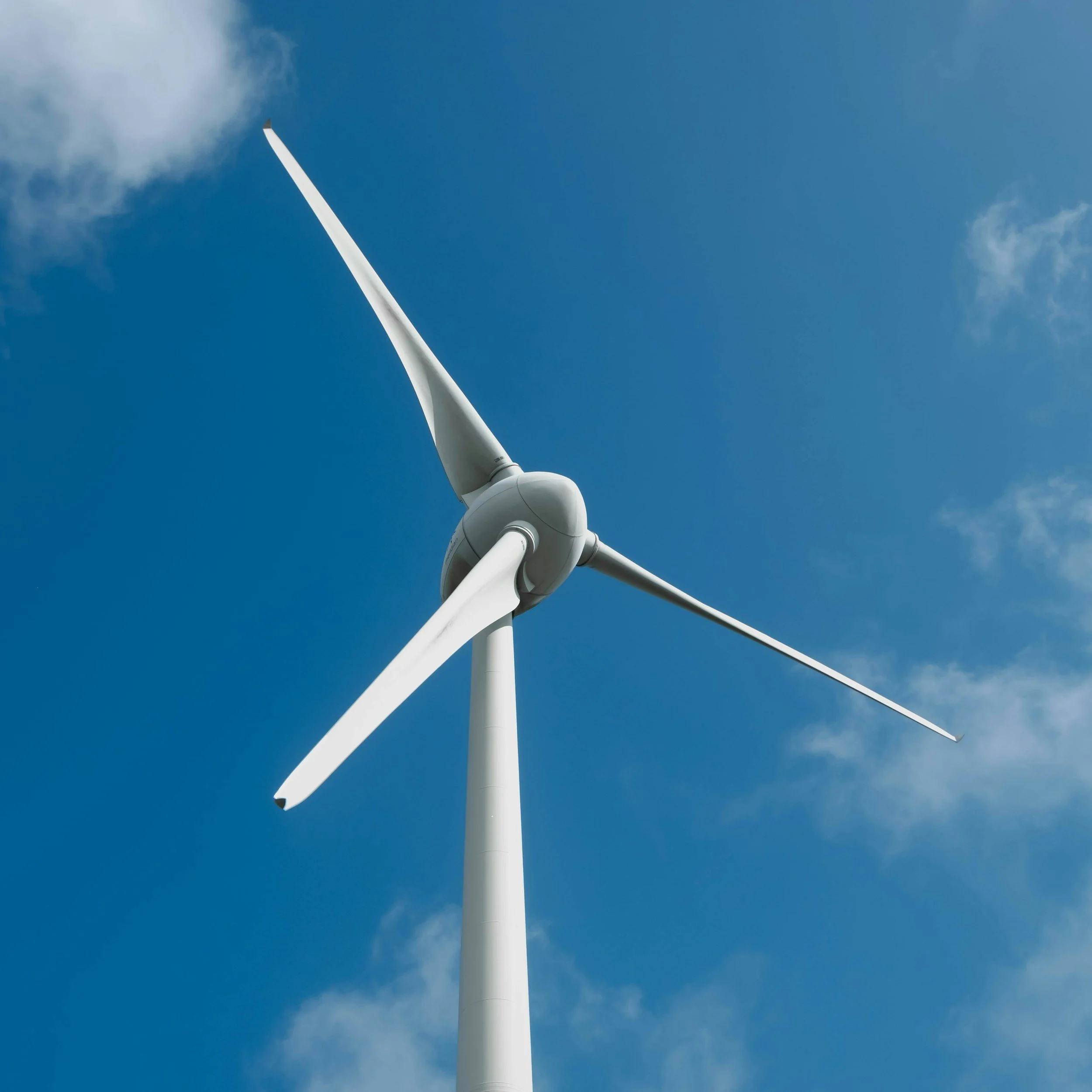 A large white wind turbine standing against a clear blue sky with a few small clouds.
