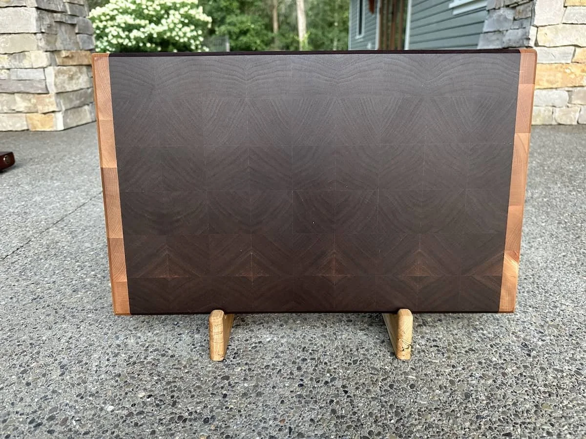 A wooden stereo speaker with a geometric panel design, standing on two small wooden legs outside.