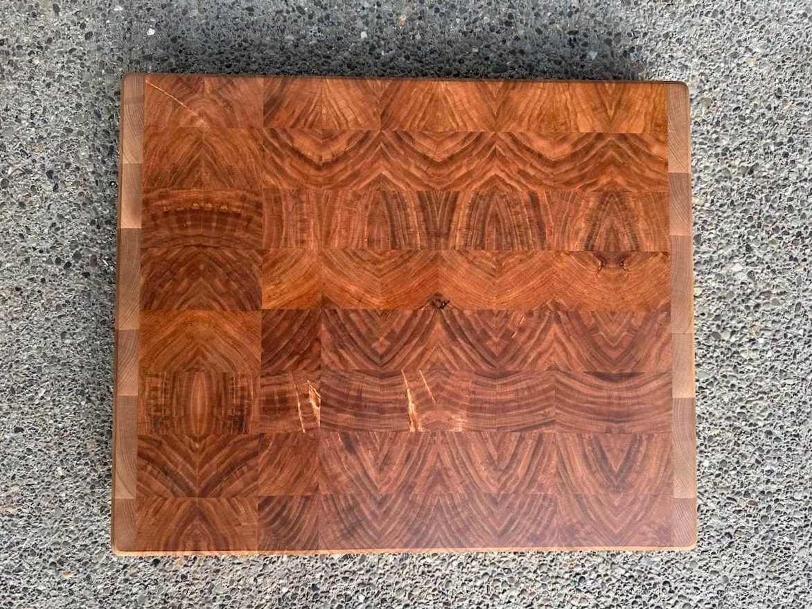 Top-down view of a wooden cutting board with a natural grain pattern, placed on a textured concrete surface.