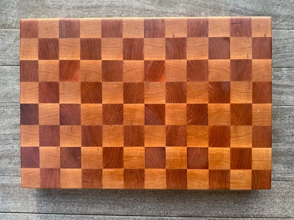 A wooden chessboard with alternating light and dark squares on a concrete surface.