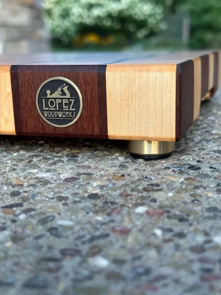 Close-up of a wooden device with a Lopez Woodworks badge, placed on a textured concrete surface outdoors.