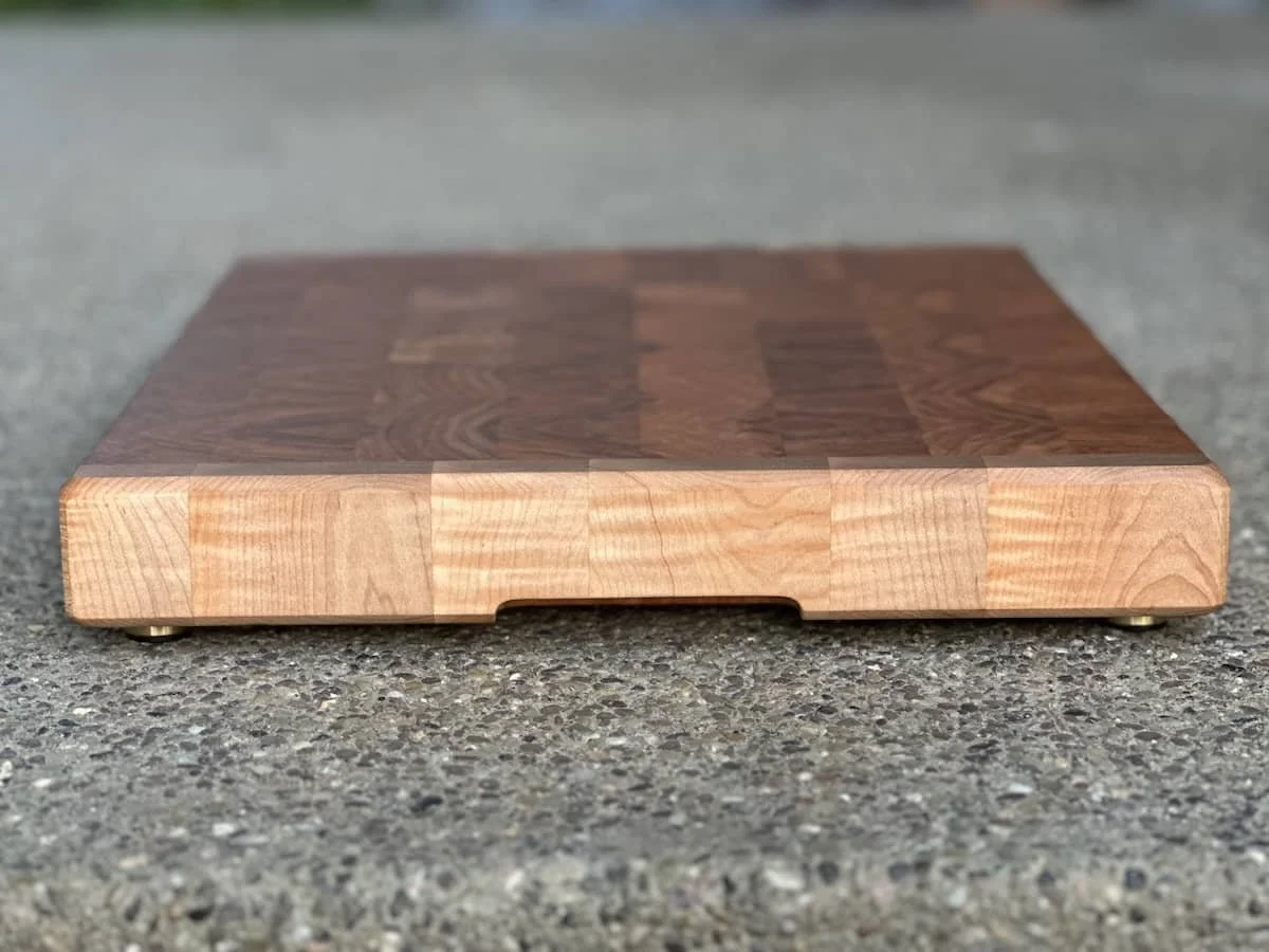 A wooden cutting board with a checkerboard pattern placed on a gray speckled surface.