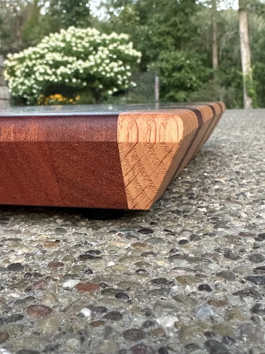 Close-up of a wooden chessboard piece on a gravel surface with trees and white flowering shrub in the background.