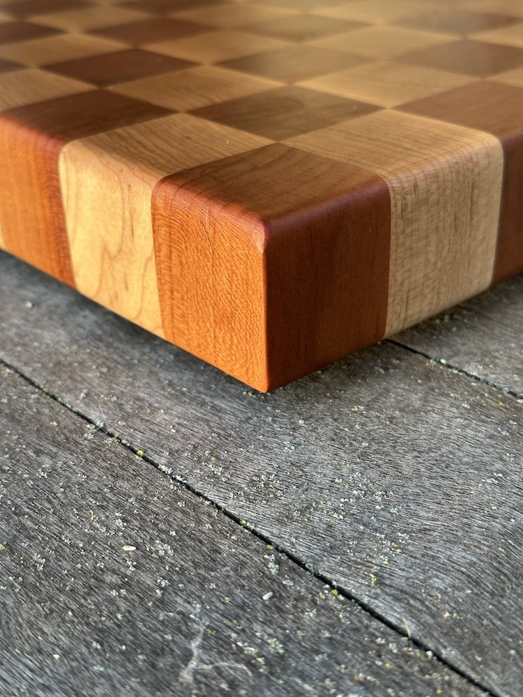 Close-up of a wooden checkerboard with alternating light and dark squares, placed on a weathered wooden surface.