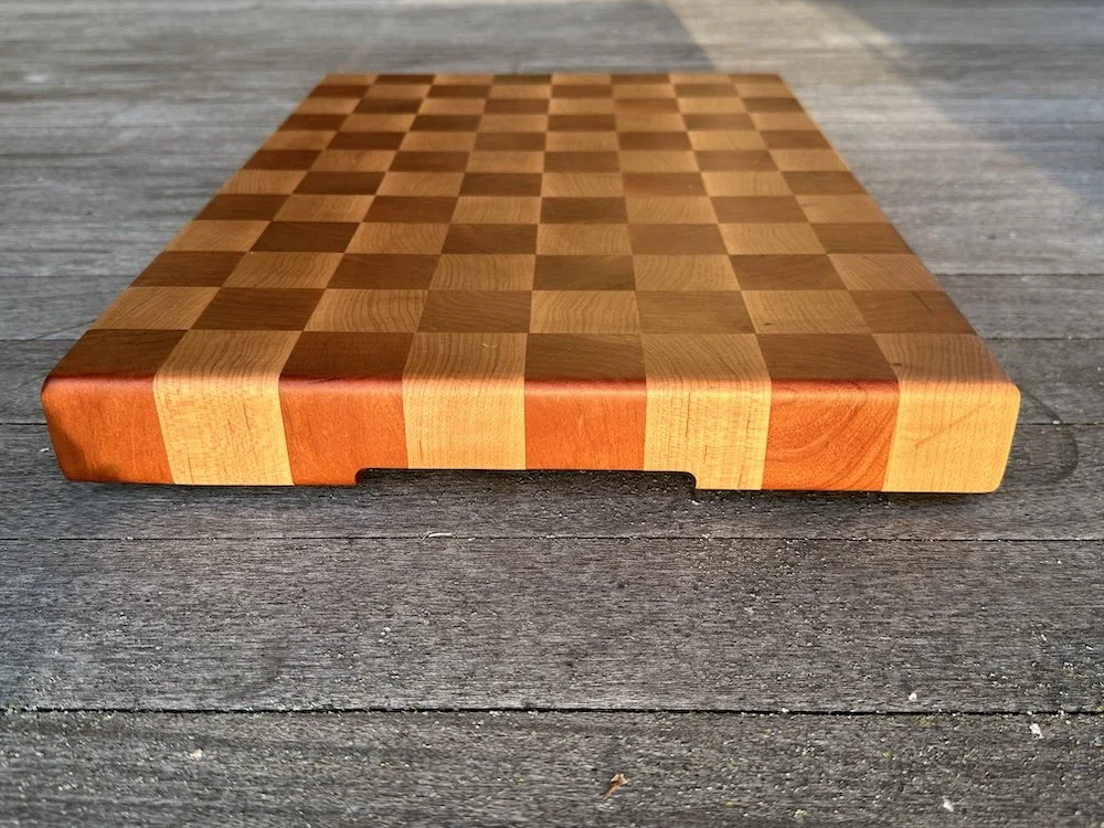 A wooden chessboard with alternating light and dark squares placed on a gray wooden surface.