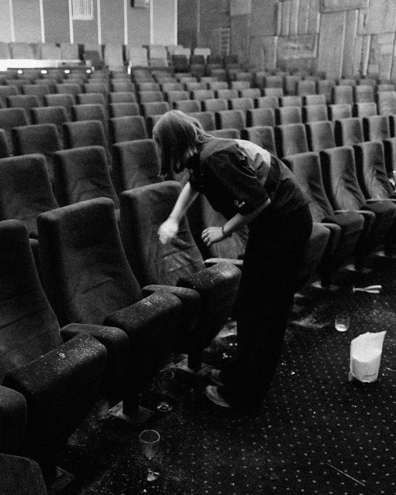 A person cleaning theater seats in a large auditorium with rows of empty chairs.