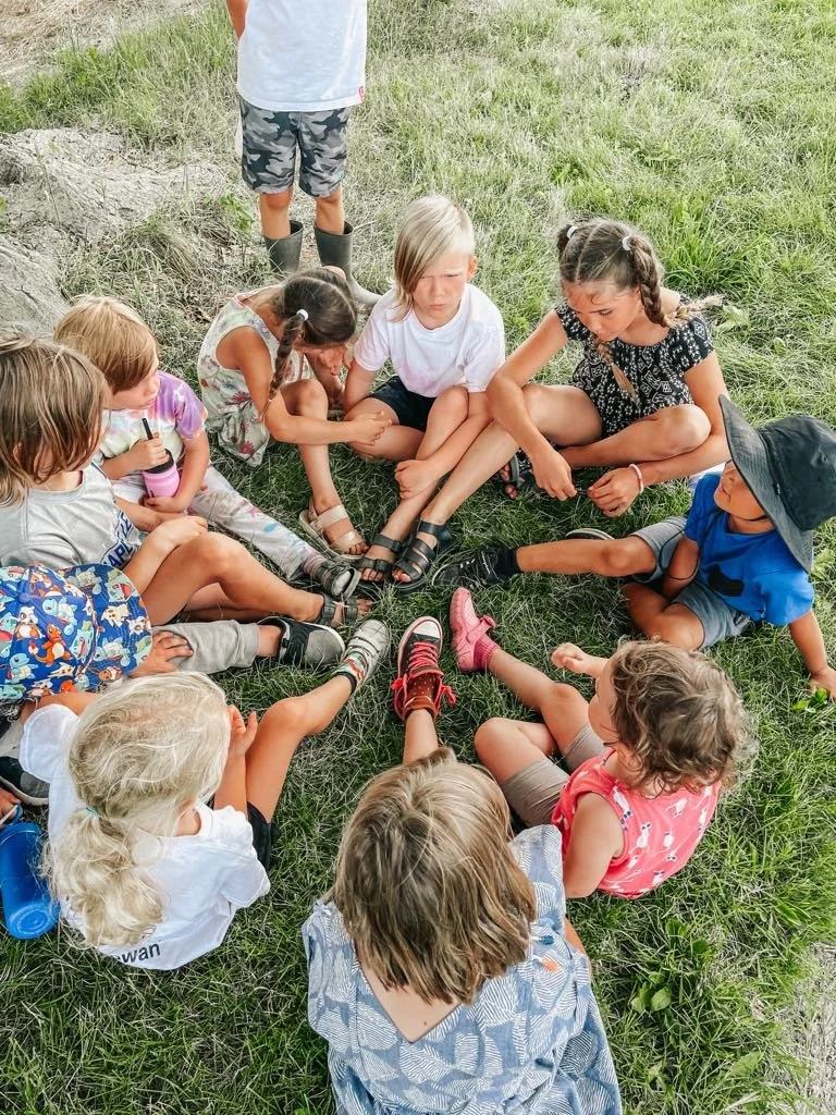 Group of children sitting in a circle on grass, holding hands.