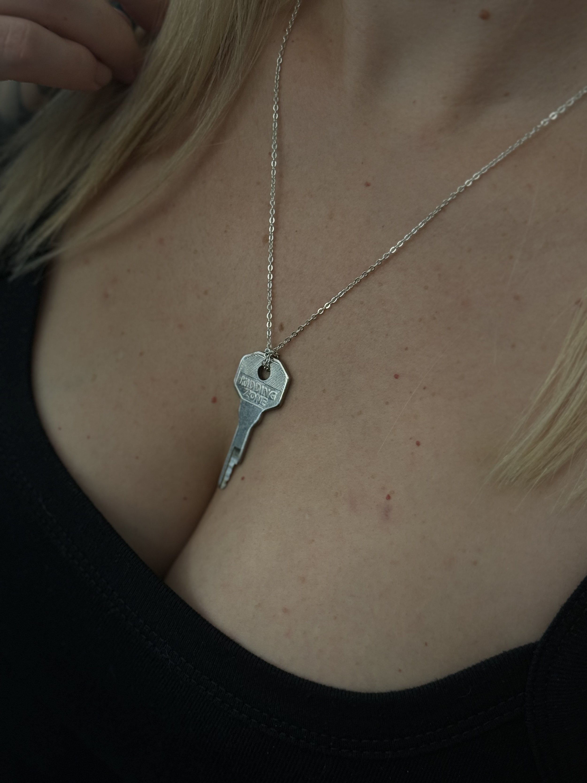 Necklace with a key pendant labeled 'DROPPING ZONE' worn by a woman with blonde hair and fair skin, wearing a black top.