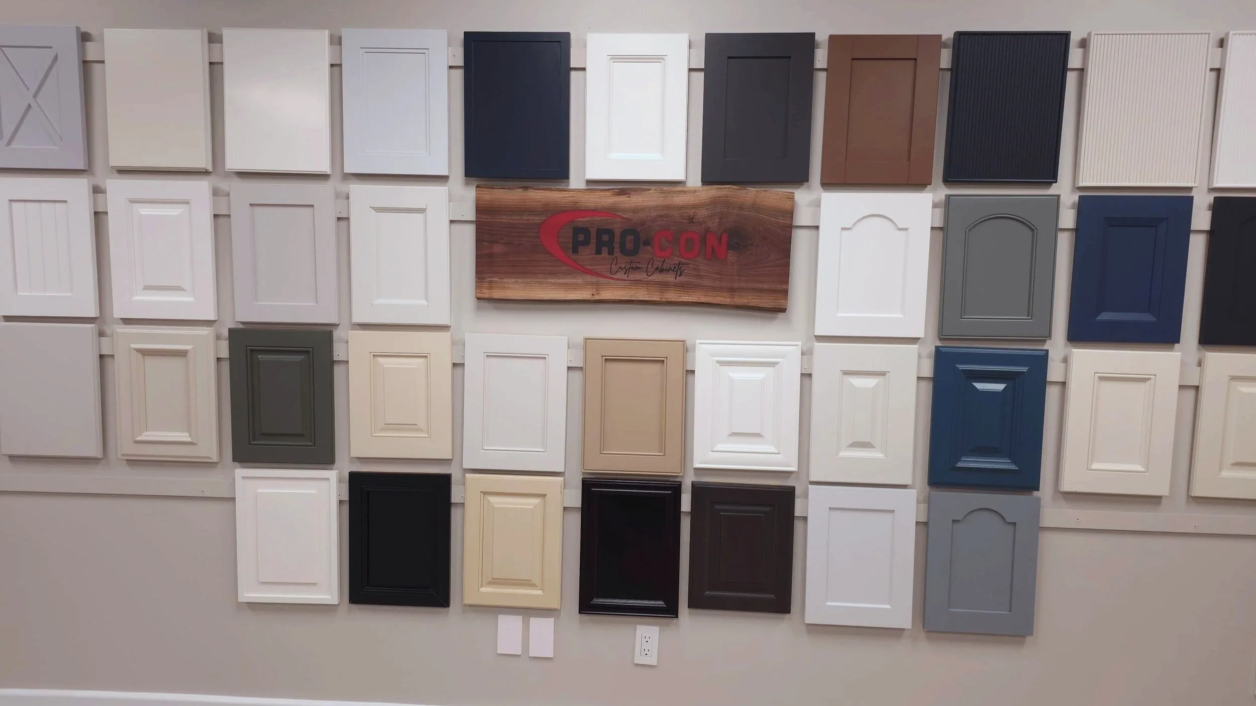 Display of various cabinet door samples in different wood finishes and colors mounted on a wall.