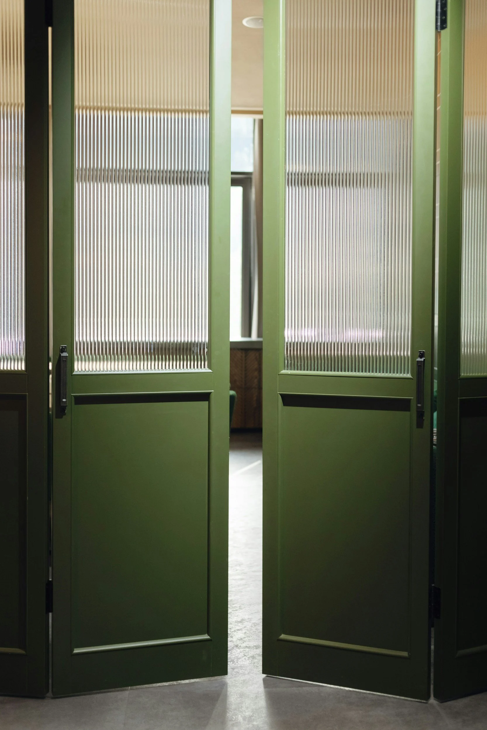 Green folding doors partially open, revealing a room with a window and beige walls.