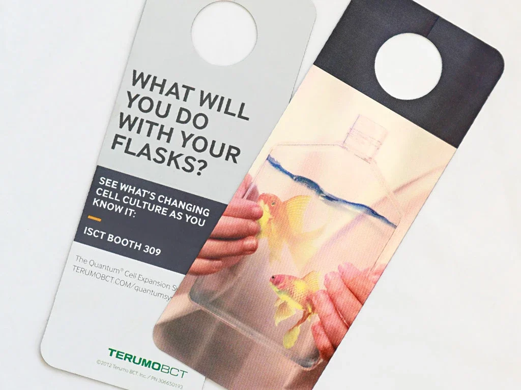 A door hanger brochure with a hanging hole at the top, promoting cell culture at a trade show booth. Featuring an alternative use for flasks, a gold fish aquarium.