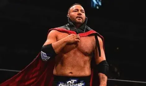 A medium shot photograph of the professional wrestler QT Marshall inside a dimly lit wrestling arena