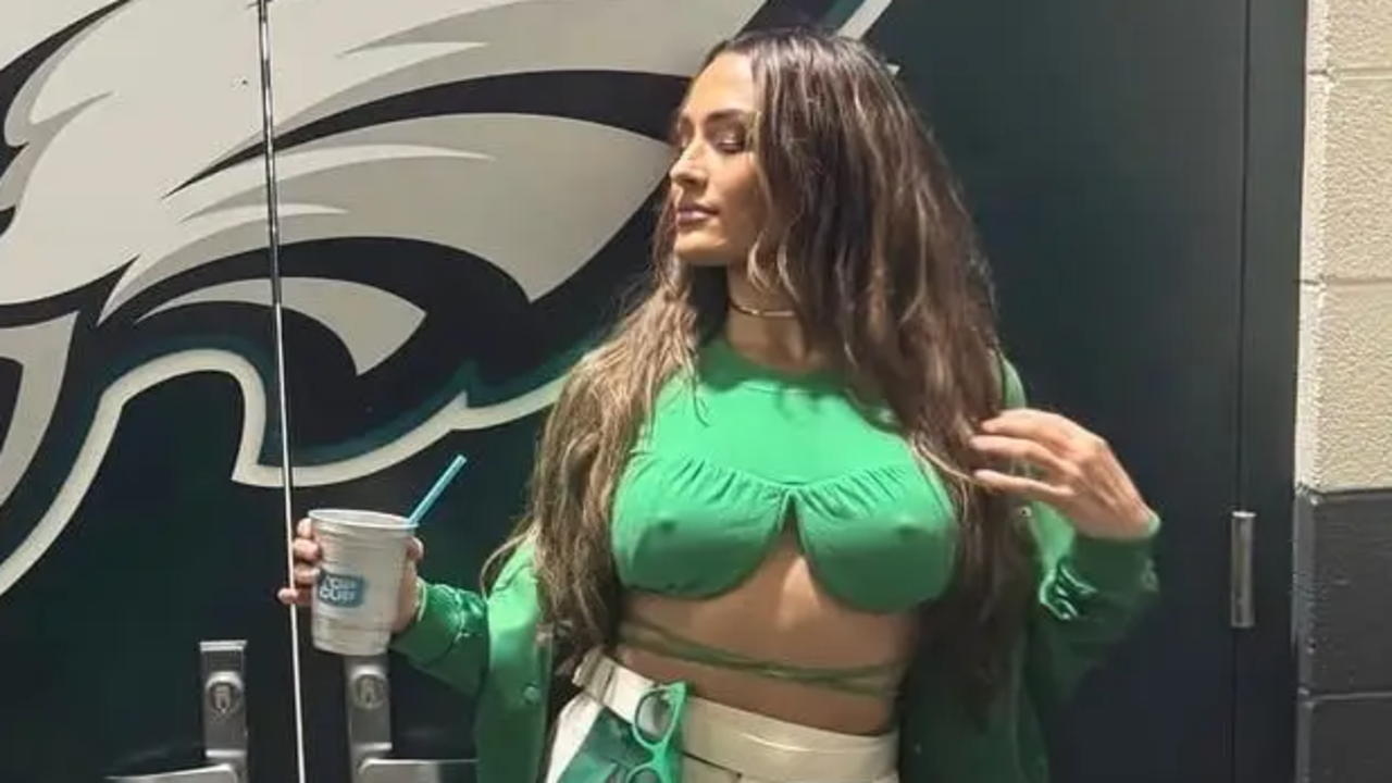 Nikki Garcia posing in front of a Philadelphia Eagles logo wearing a green top and holding a drink.