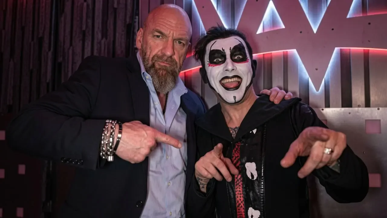"Triple H with his arm around Danhausen in full face paint, both pointing at the camera"
