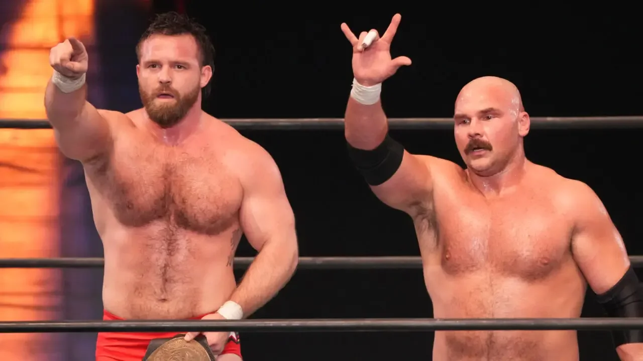 FTR, Dax Harwood and Cash Wheeler, standing in the center of an AEW ring under spotlights, holding up their signature "Top Guys" hand gestures.
