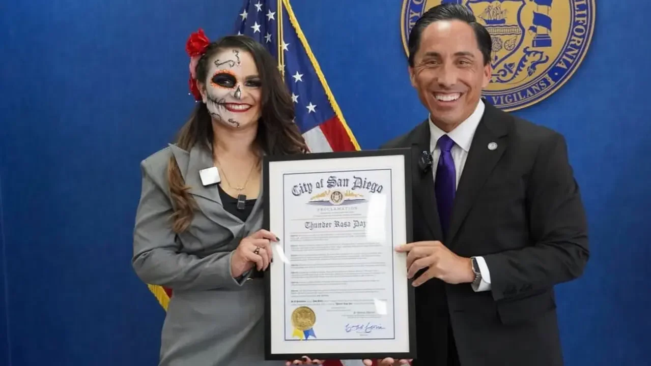 Thunder Rosa, wearing her signature Catrina face paint and a grey suit, stands alongside smiling San Diego Mayor Todd Gloria