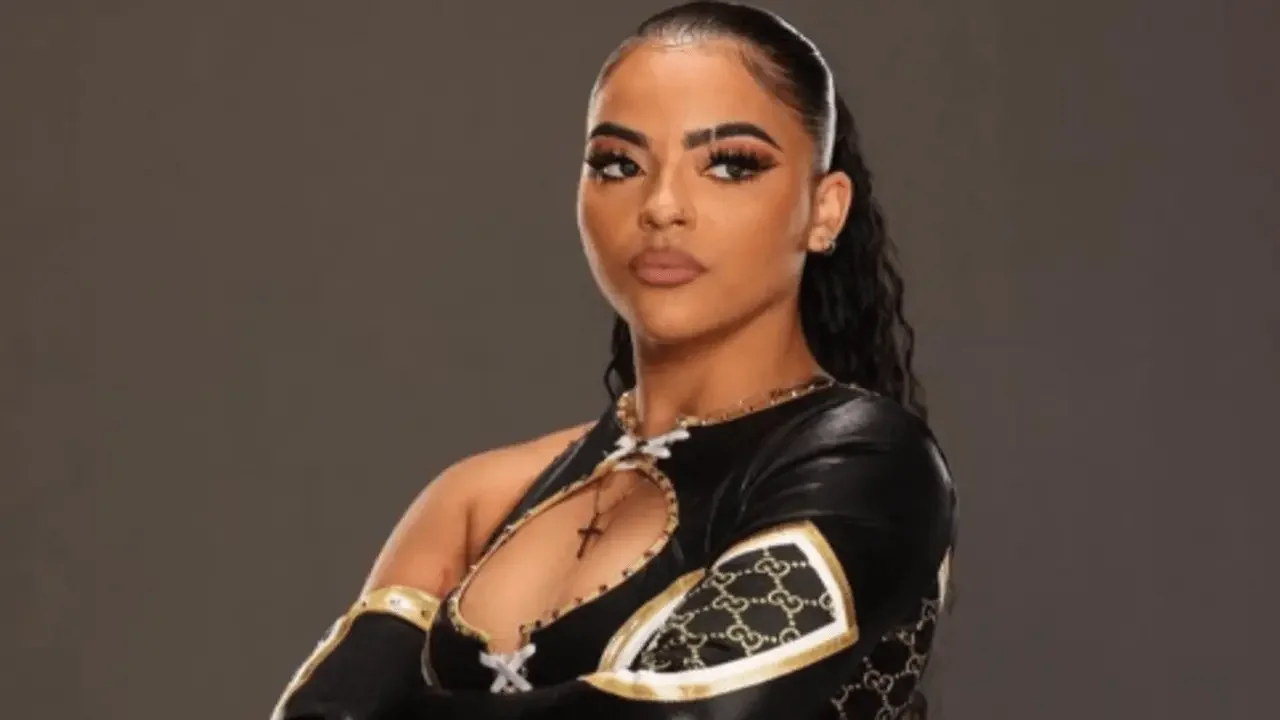 Jaida Parker posing with arms crossed in a black and gold Gucci-patterned wrestling outfit, looking confidently at the camera.
