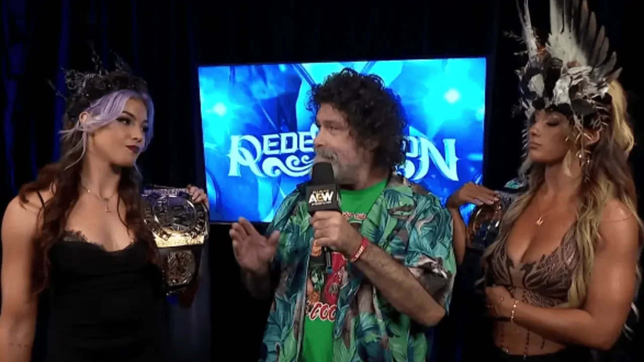 Professional wrestling legend Mick Foley holds an AEW microphone while speaking between Lena Kross, wearing a black dress and crown with purple-tinted hair, and Megan Bayne.