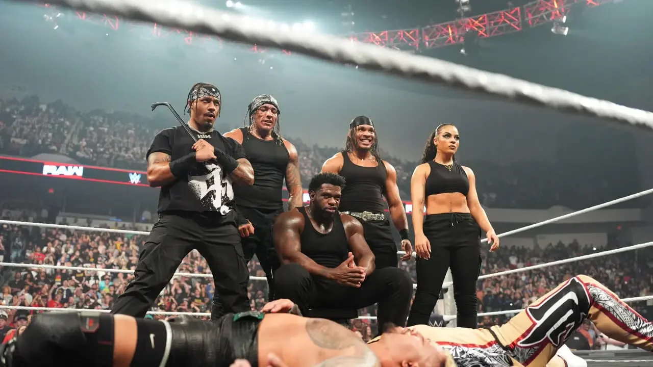 The 946 faction standing dominantly in the ring on WWE Raw over defeated opponents.