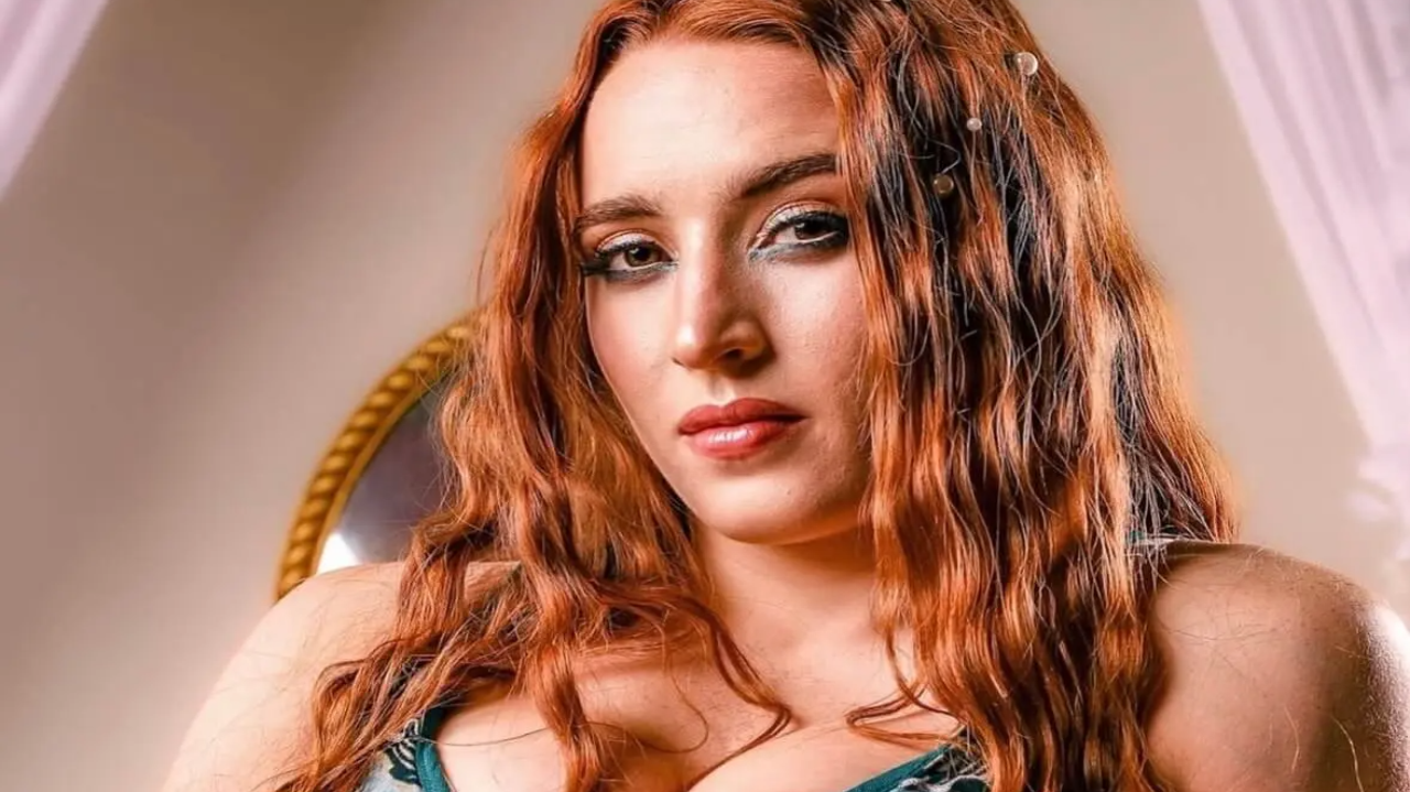 Professional wrestler Sloane Jacobs looking into the camera with long wavy red hair and blue eye makeup in a close-up portrait.